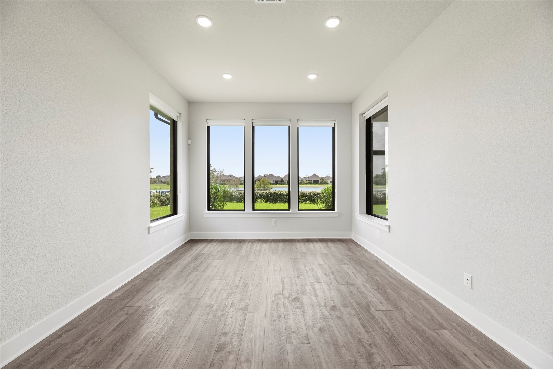 Versatile guest suite boasting warm wood-plank flooring, recessed lighting, and panoramic views of the neighborhood lake through large picture windows.