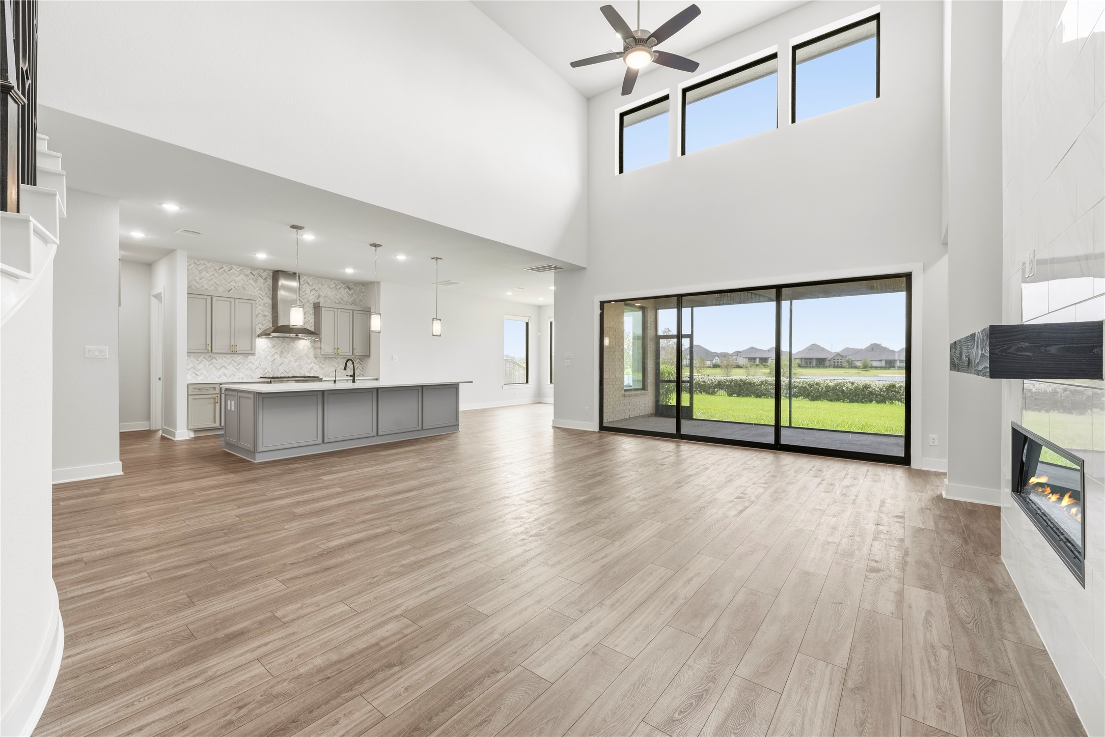 Breathtaking open-concept living area featuring soaring two-story ceilings, wall of glass sliding doors to the patio, modern tile fireplace, and direct flow to the gourmet kitchen.