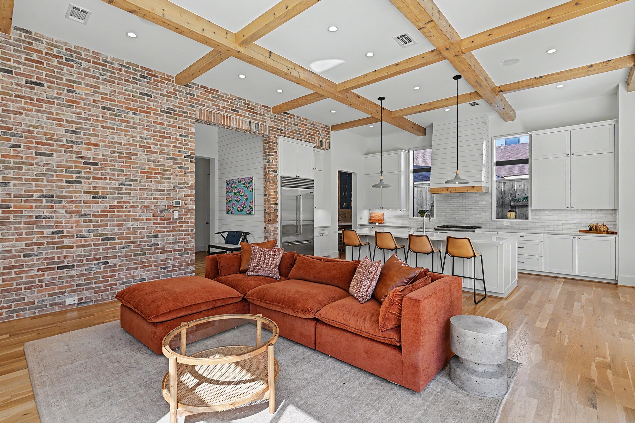 A textured brick accent wall and light-stained cedar beams add warmth and character to the sophisticated living space.