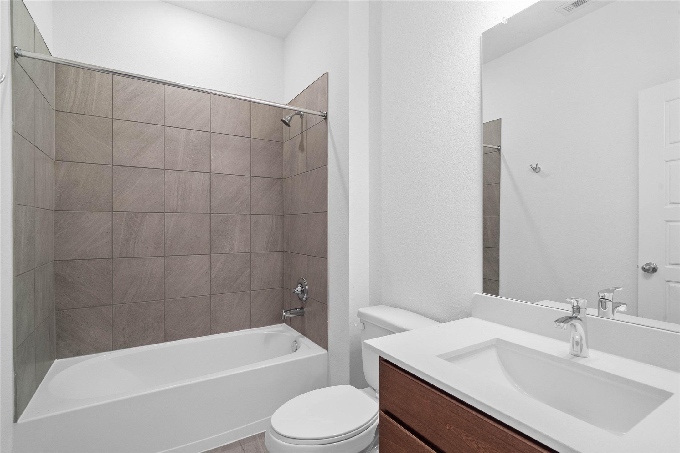 The secondary bathroom showcases tile flooring, a bath/shower combo with a Daltile tile surround, a 30" vanity with a stunning light countertop, a mirror, sleek fixtures, and contemporary finishes throughout.