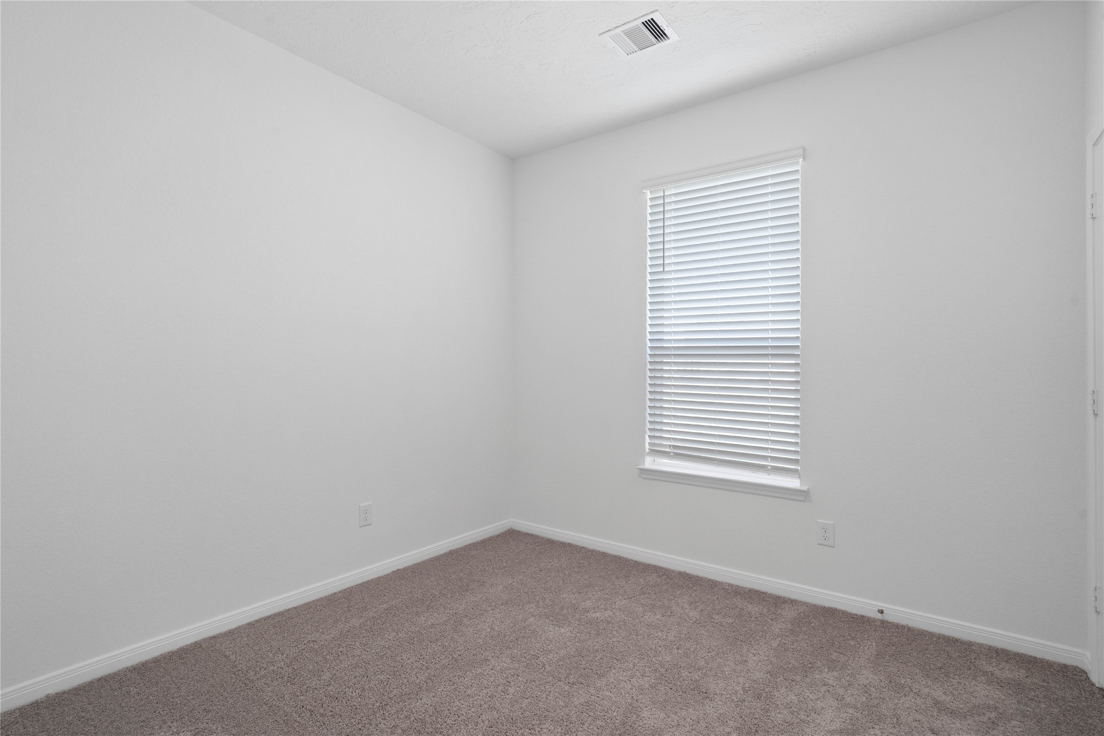 This secondary bedroom offers comfort and style with plush carpeting, neutral paint tones, recessed lighting, a large window with blinds, and a generously sized closet.