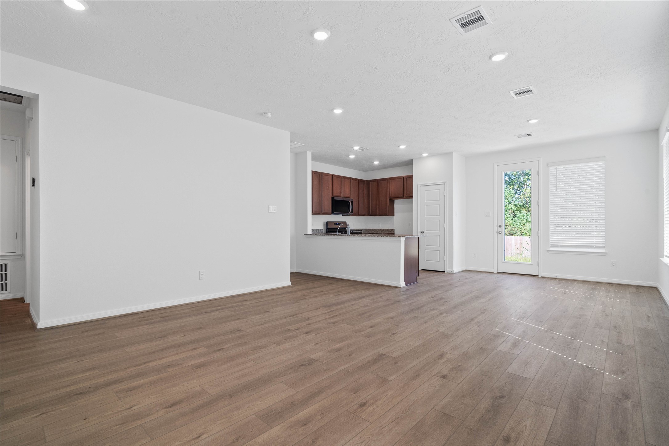 This bright and airy Great Room offers a spacious layout ideal for both relaxing evenings and lively gatherings. Designed for comfort and connection, it features vinyl plank flooring, large window with blinds, high ceilings, recessed lighting, and seamless access to the stunning kitchenperfect for everyday living and entertaining alike.