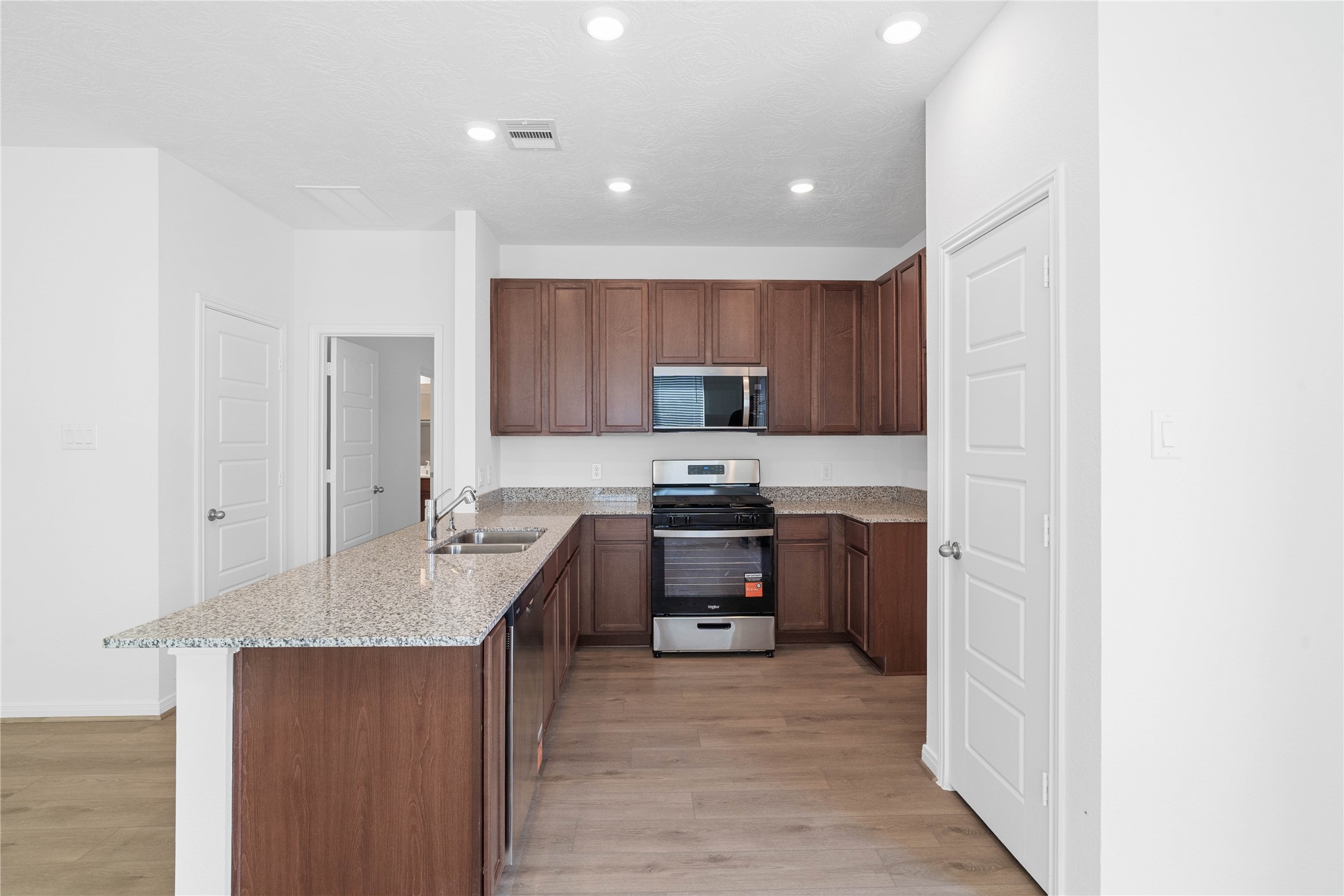The kitchen boasts high ceilings, recessed lighting, Woodmont Cody cabinets in a Ginger stain, granite countertops in Iberian White, stainless steel Whirlpool appliances, a modern Daltile backsplash, and a pantryall overlooking the Great Room.
