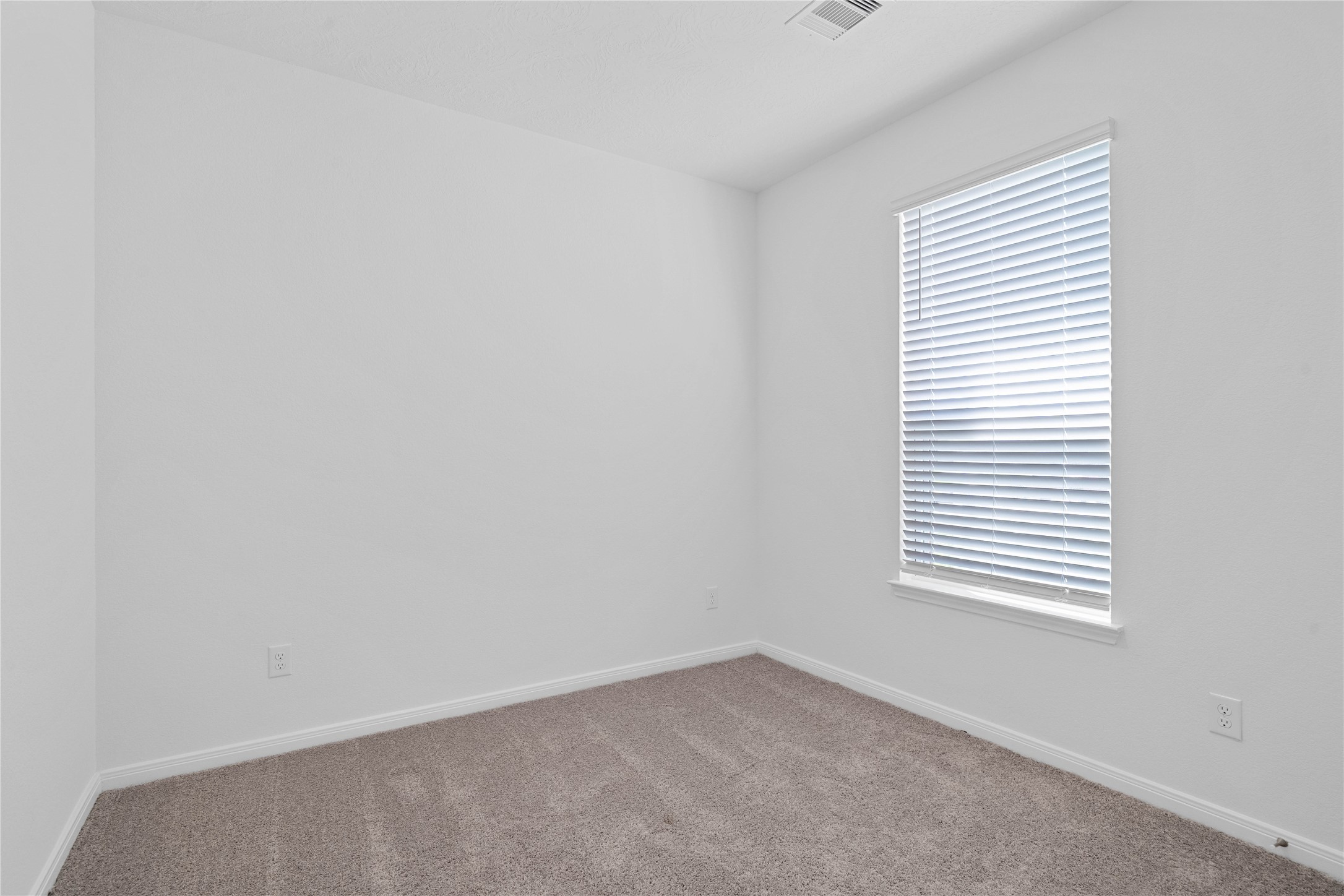 Tucked peacefully in the front of this home is this secondary bedroom. It offers comfort and style with plush carpeting, neutral paint tones, recessed lighting, a large window with blinds, and a generously sized closet.