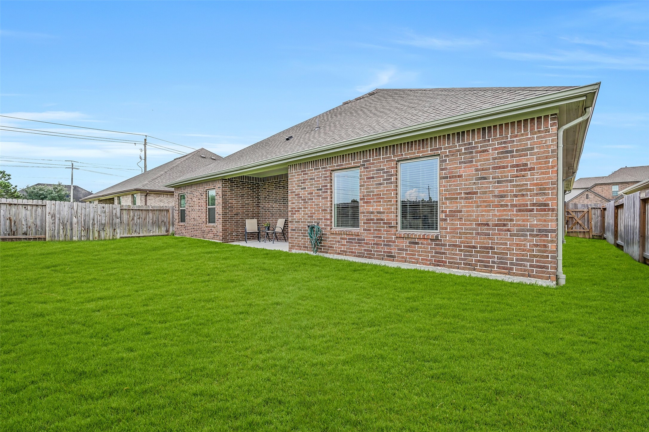 A final view showcases the home's brick rear exterior, covered patio and expansive lawn, with multiple rear-facing windows connecting the light-filled interior living spaces to the backyard.