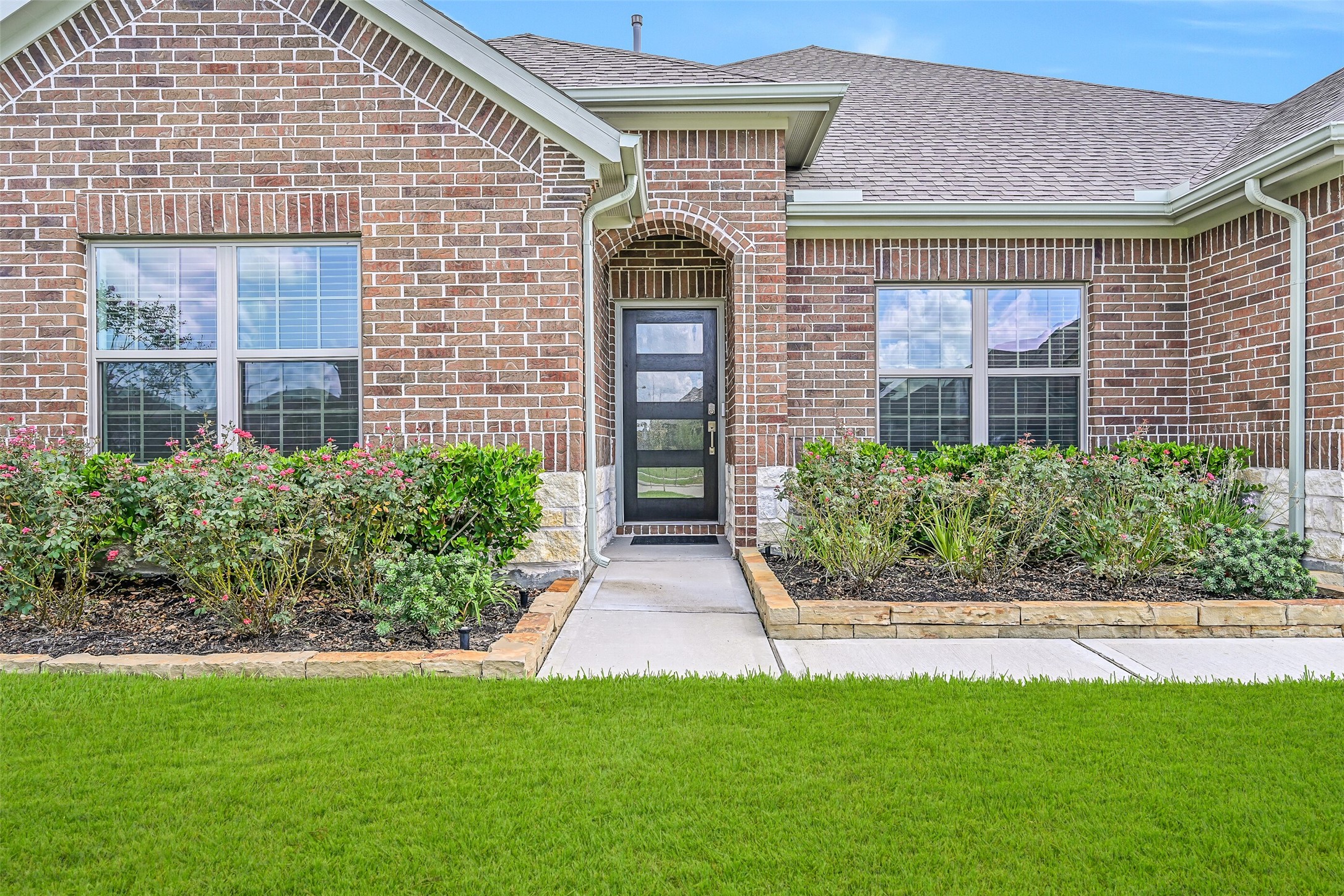 A closer look at the inviting front elevation showcases colorful established landscaping, brick & Austin limestone details and a recessed arched entry with a southwest facing contemporary style glass-panel front door.