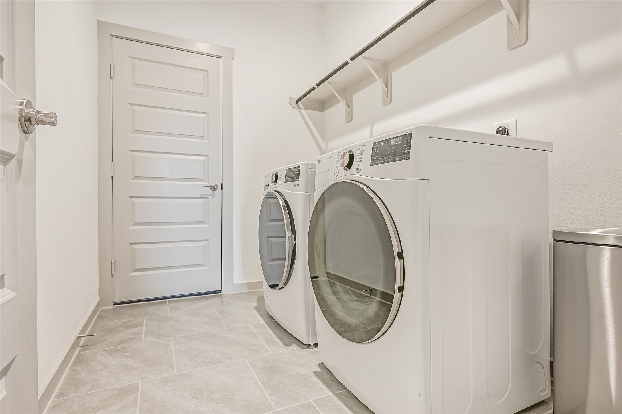 The spacious interior utility room accommodates full-size side-by-side laundry appliances and features easy-care tile flooring plus a long shelf and hanging rod for added storage and functionality.