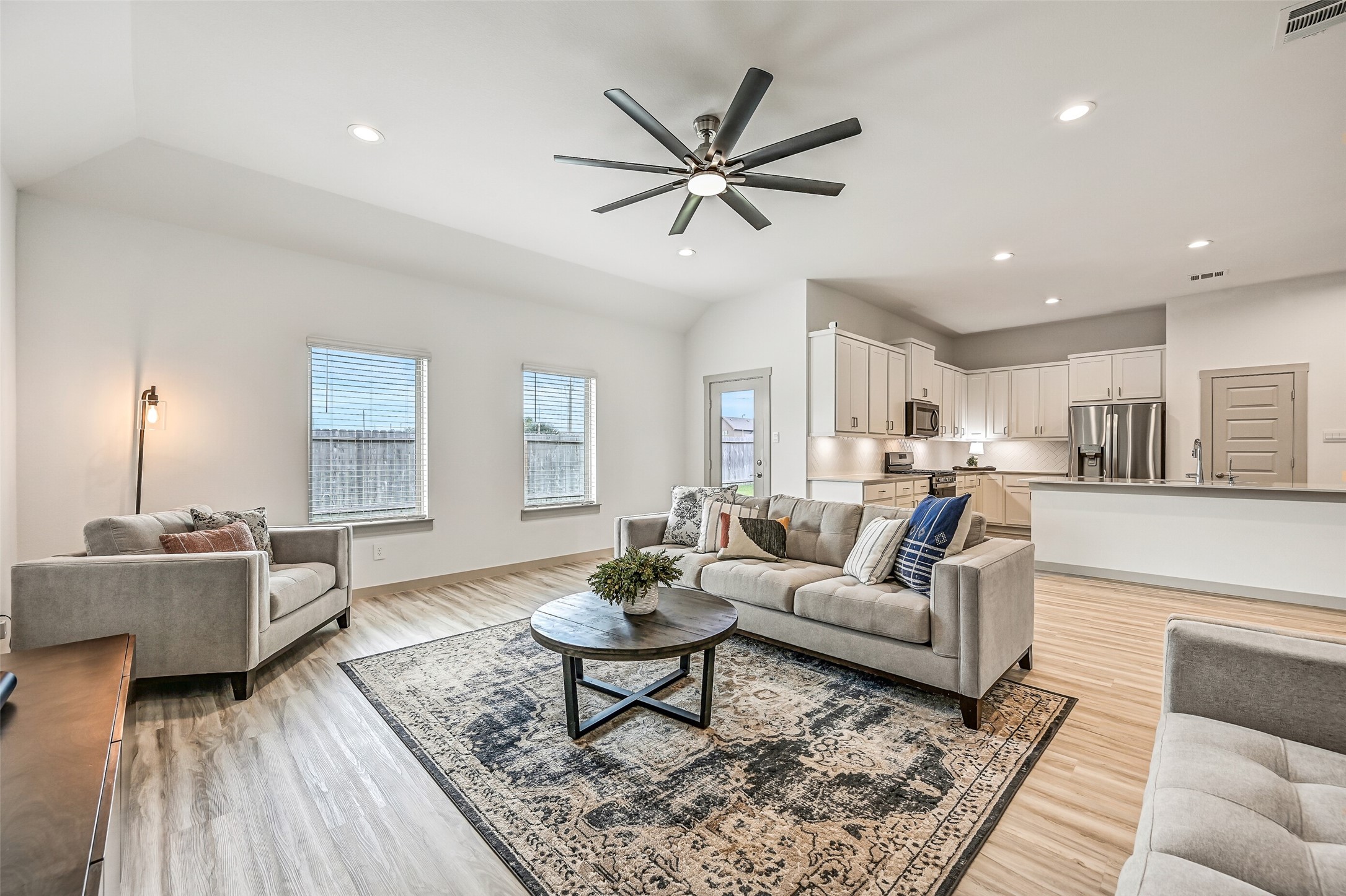Abundant natural light fills the spacious family room through multiple rear-facing windows, while an oversized ceiling fan and neutral finishes complement the home's fresh contemporary style.