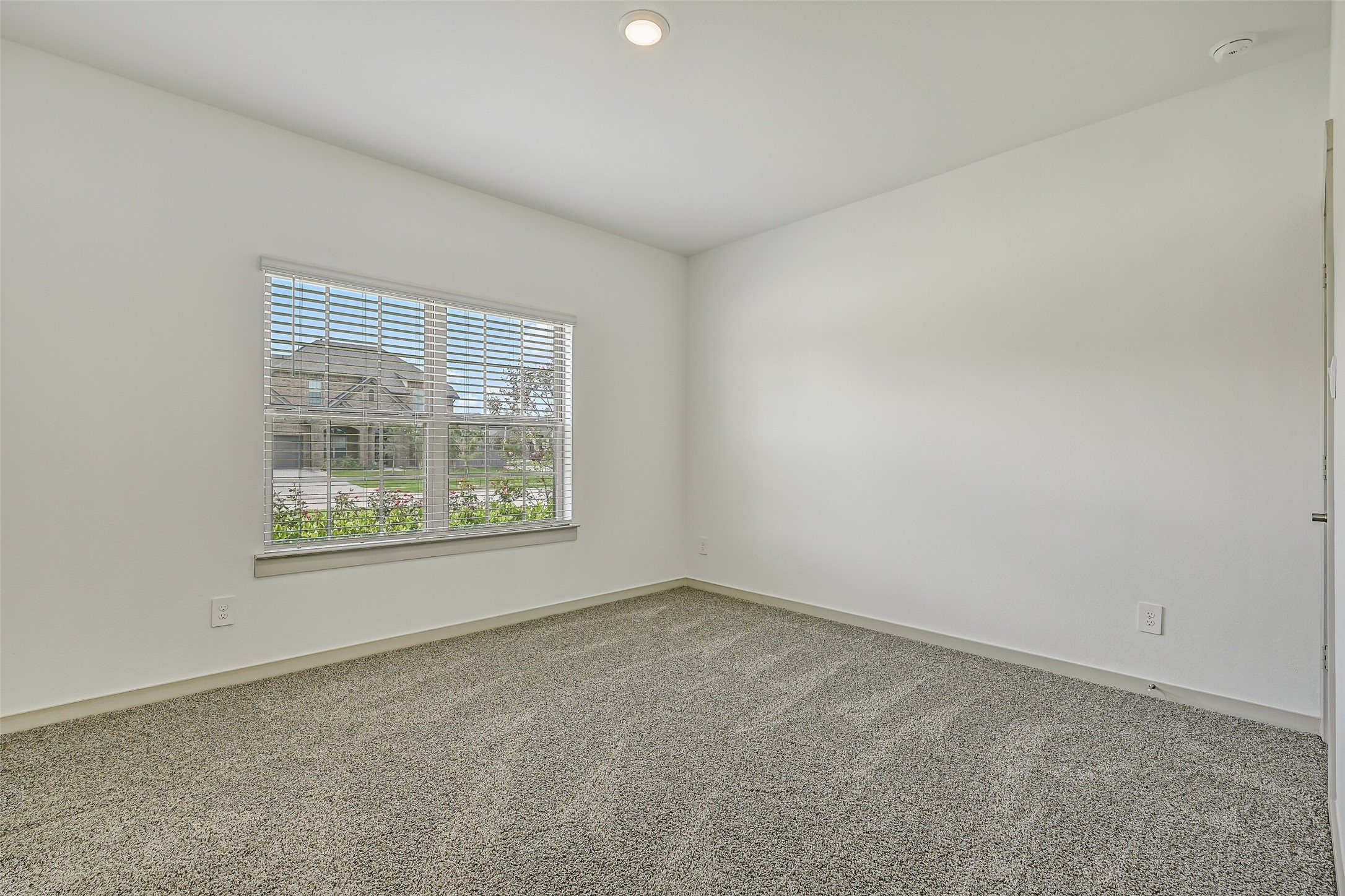 Another secondary bedroom offers plush neutral carpet, a large front-facing window and a versatile blank canvas ready to accommodate a variety of furnishings and uses.