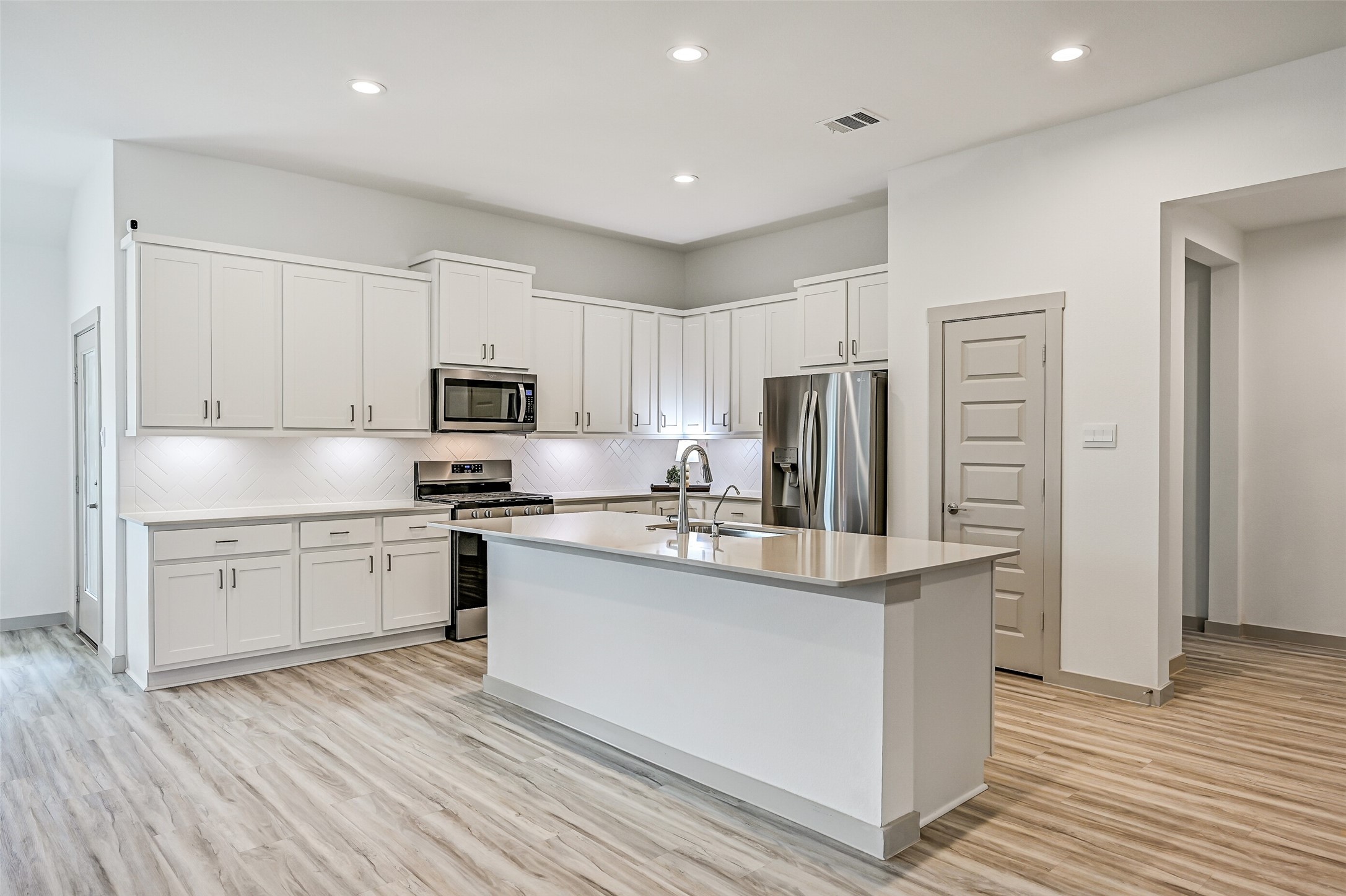 Crisp white cabinetry stretches across the kitchen, complemented by sleek countertops, stainless appliances and a herringbone-pattern tile backsplash. The oversized island adds an abundance of prep space and storage.
