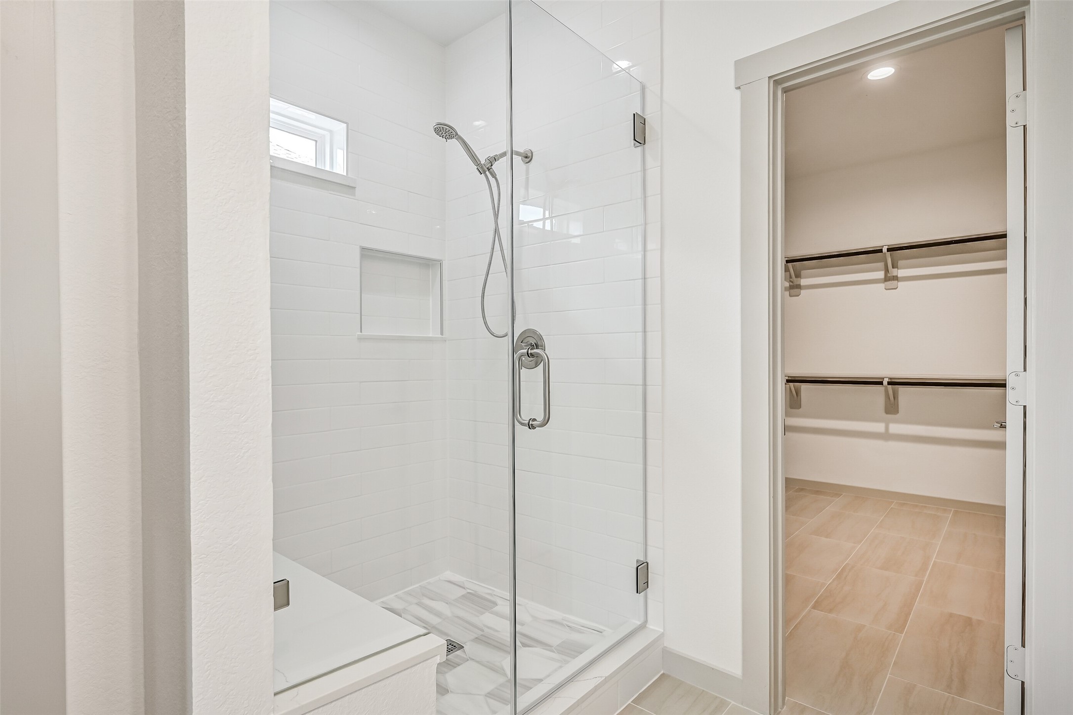 An oversized frameless glass shower showcases crisp tile surrounds, a built-in niche, handheld showerhead and natural light, creating a clean contemporary focal point in the primary bath.