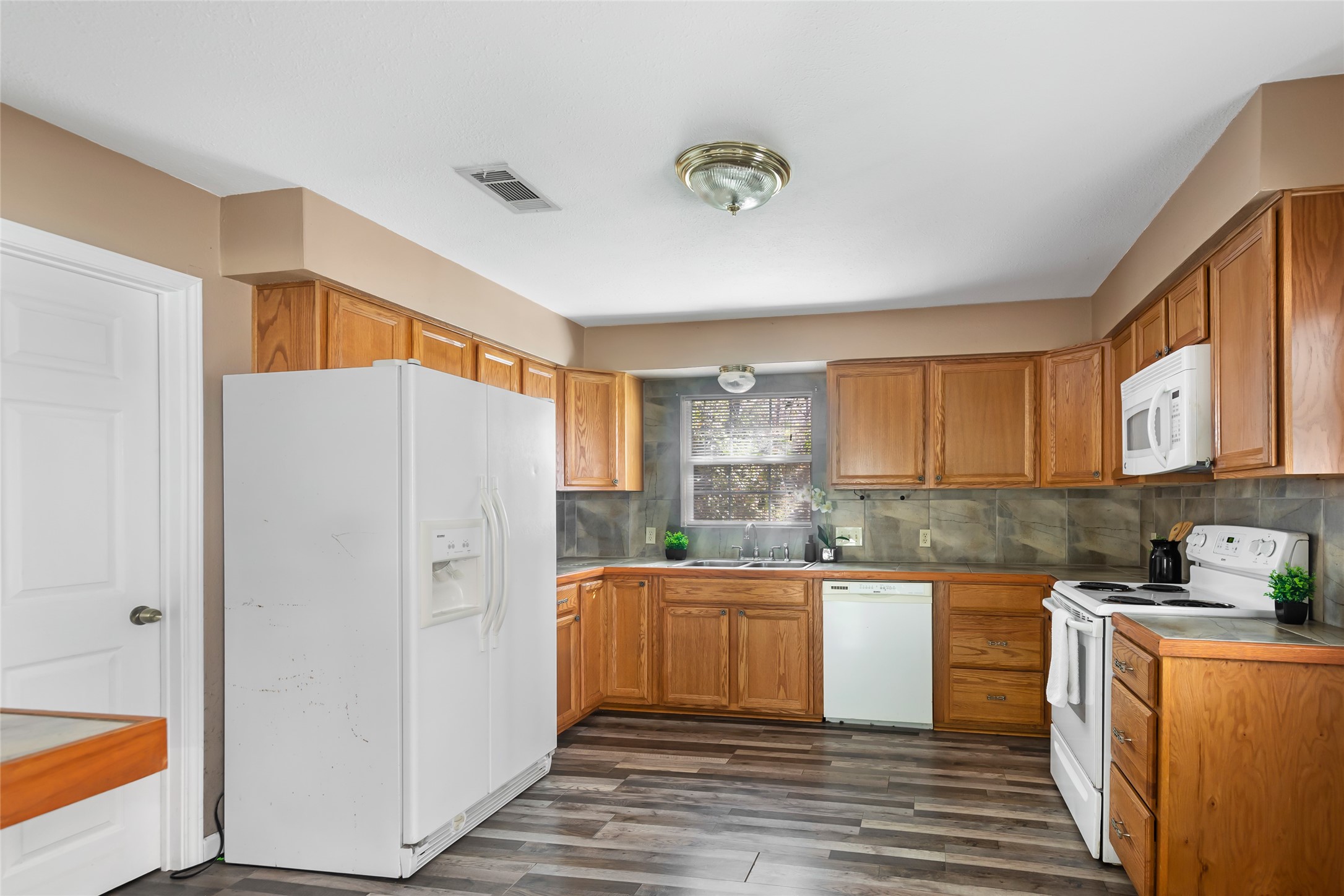 Functional kitchen with ample cabinetry, white appliances and wood-look flooring.
