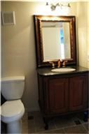This bathroom features a classic vanity with a dark countertop, an elegant framed mirror, and a toilet. The lighting is warm, enhancing the cozy feel.