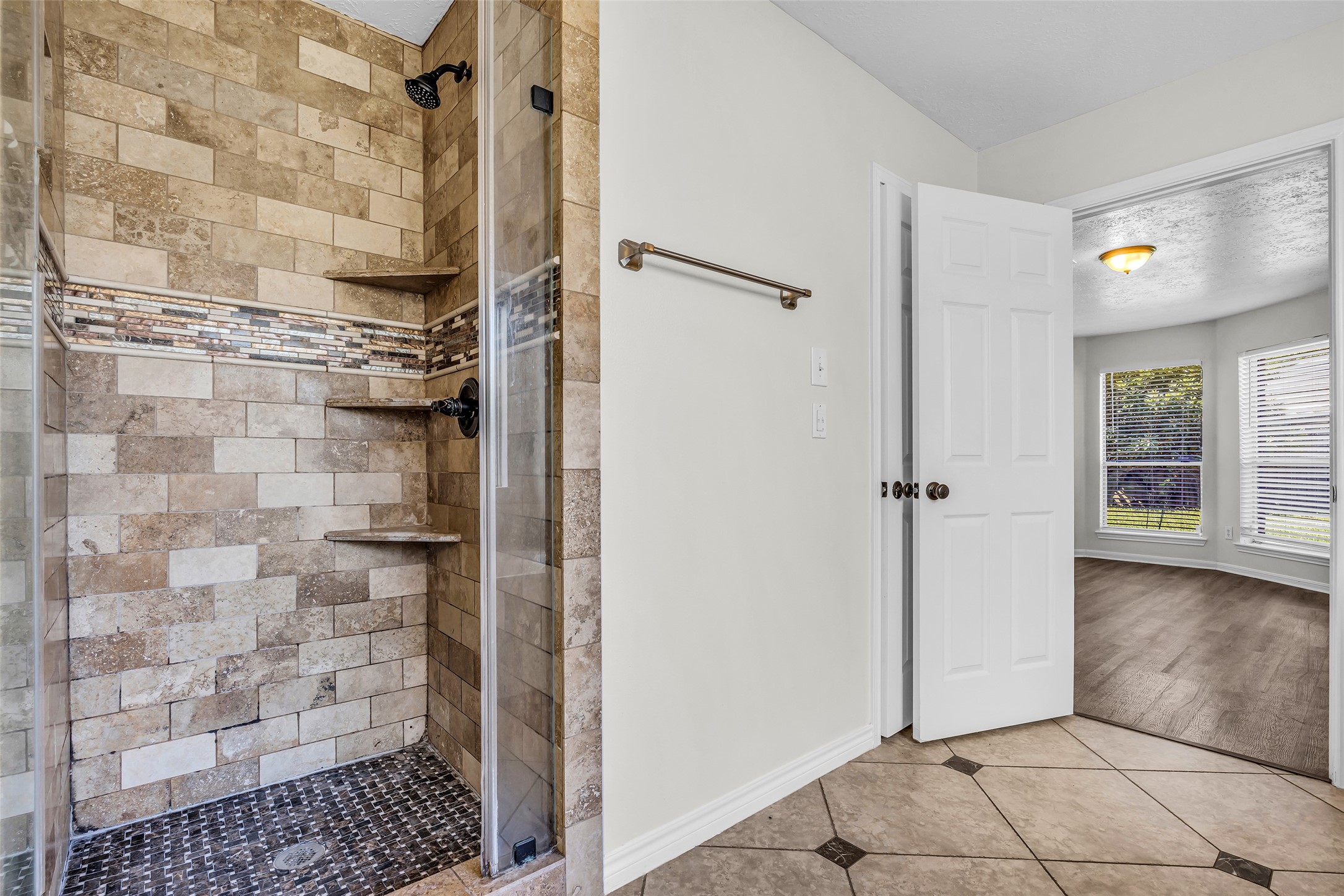 A walk-in shower with stone-look tile, built-in shelves and a glass door.