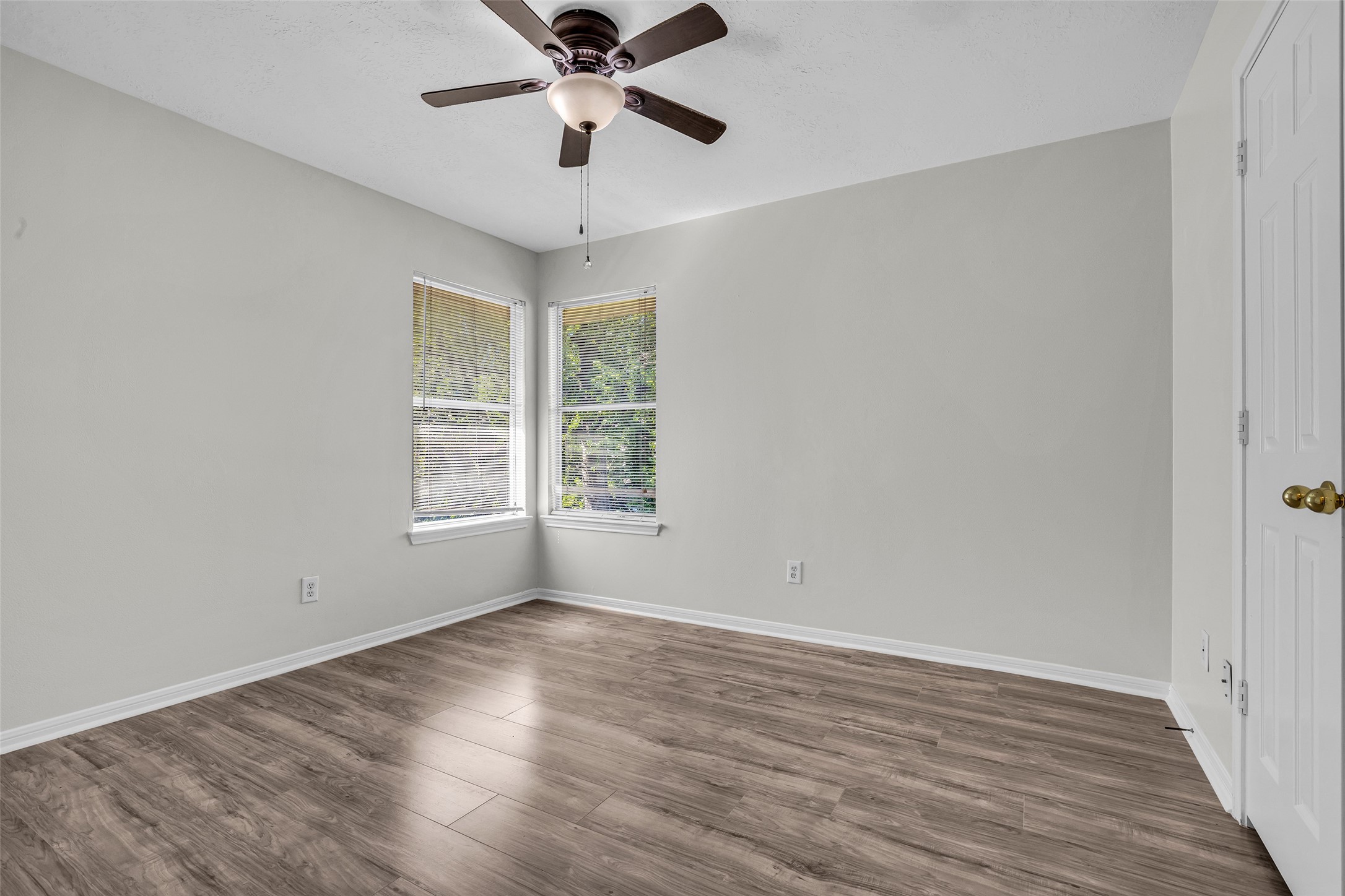 A secondary bedroom with a ceiling fan and corner windows, ready for guests.