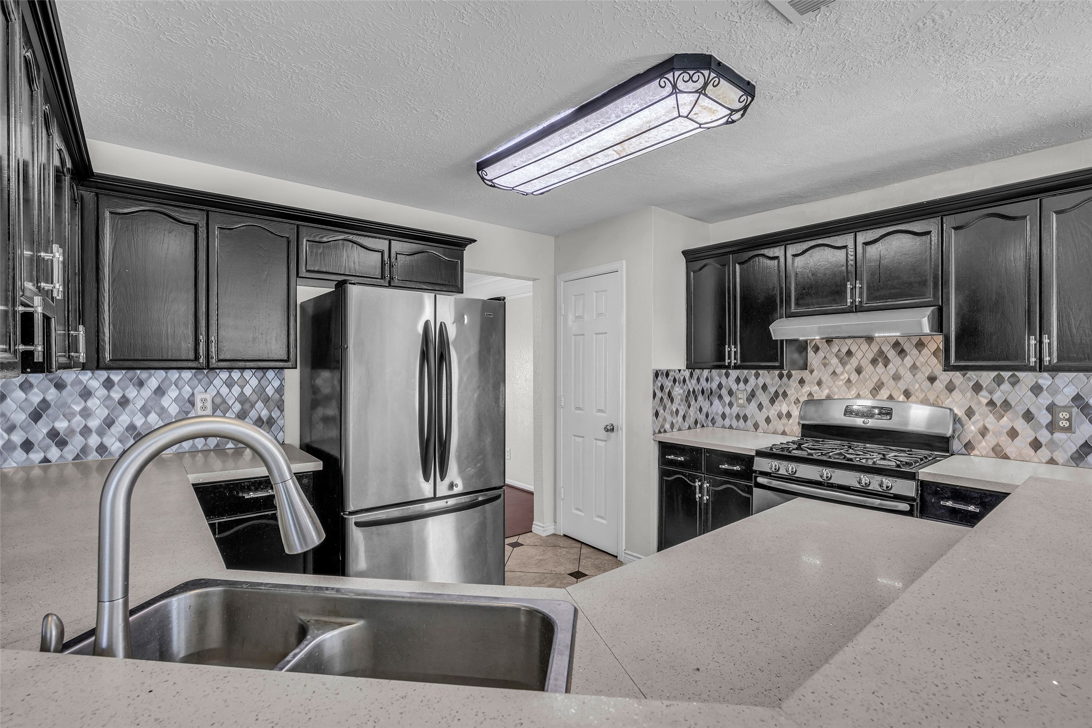 Cook in style with espresso cabinetry, a mosaic tile backsplash, a gas range and stainless steel appliances.