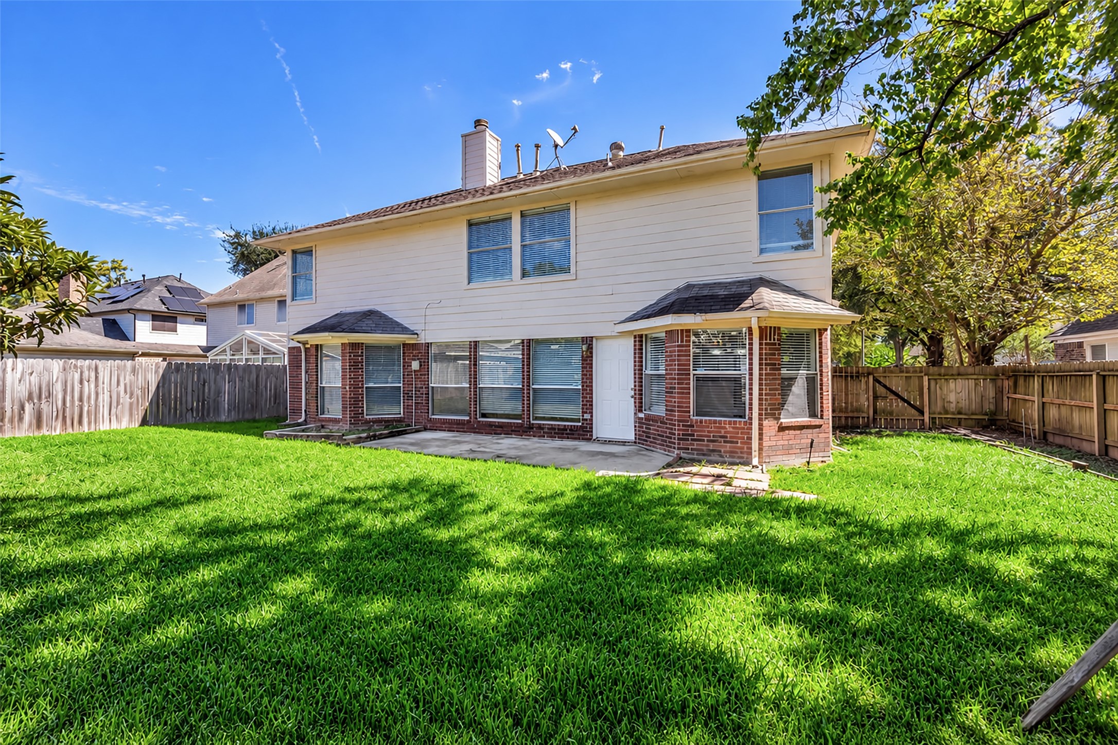 A fenced backyard with a patio and plenty of green space for outdoor fun.