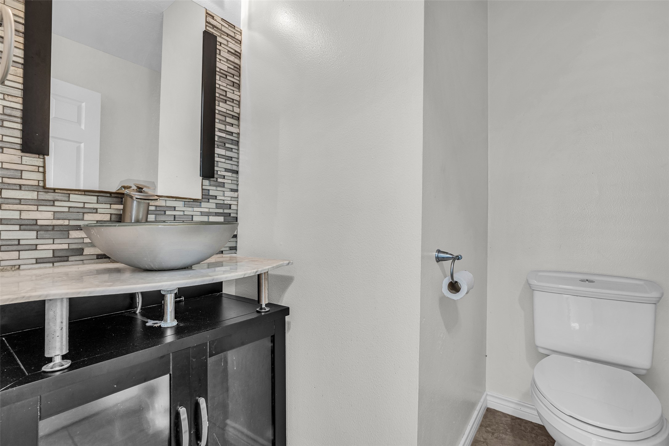 A downstairs half bath with a vessel sink and mosaic tile accent wall.