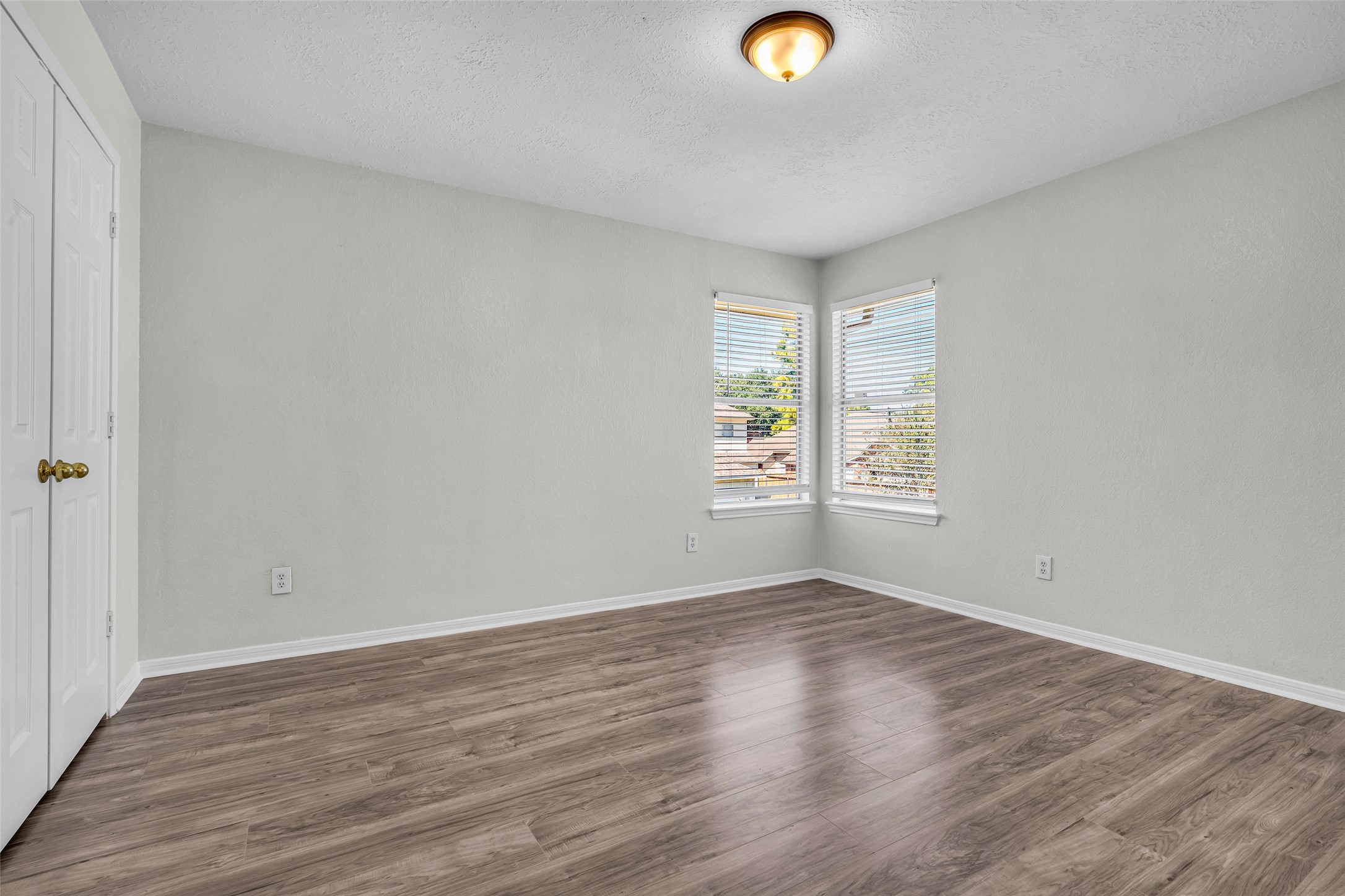 A bright secondary bedroom with two windows and wood-look flooring.