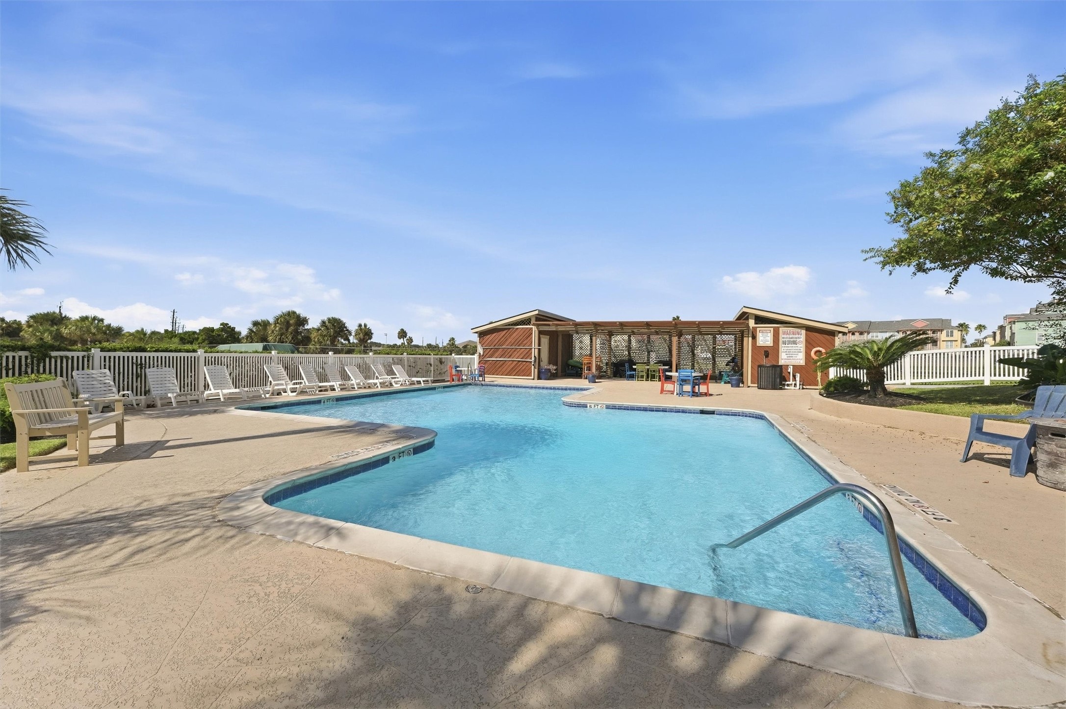 Relax and unwind in this inviting outdoor pool area, featuring a spacious deck with plenty of loungers and a cozy clubhouse for refreshments.