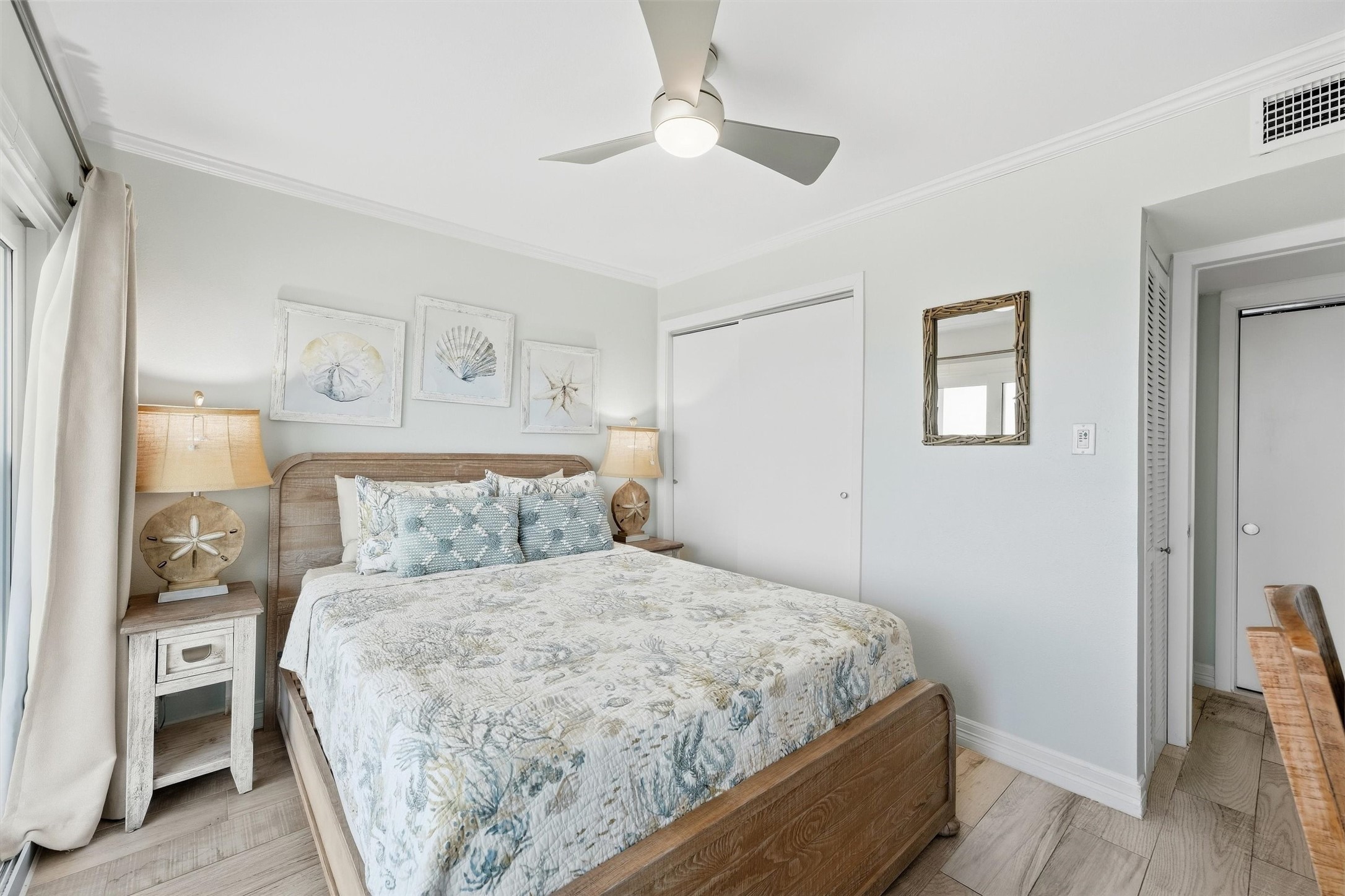 Cozy bedroom featuring a comfortable bed with coastal-themed decor, soft lighting from matching lamps, and a ceiling fan for comfort.