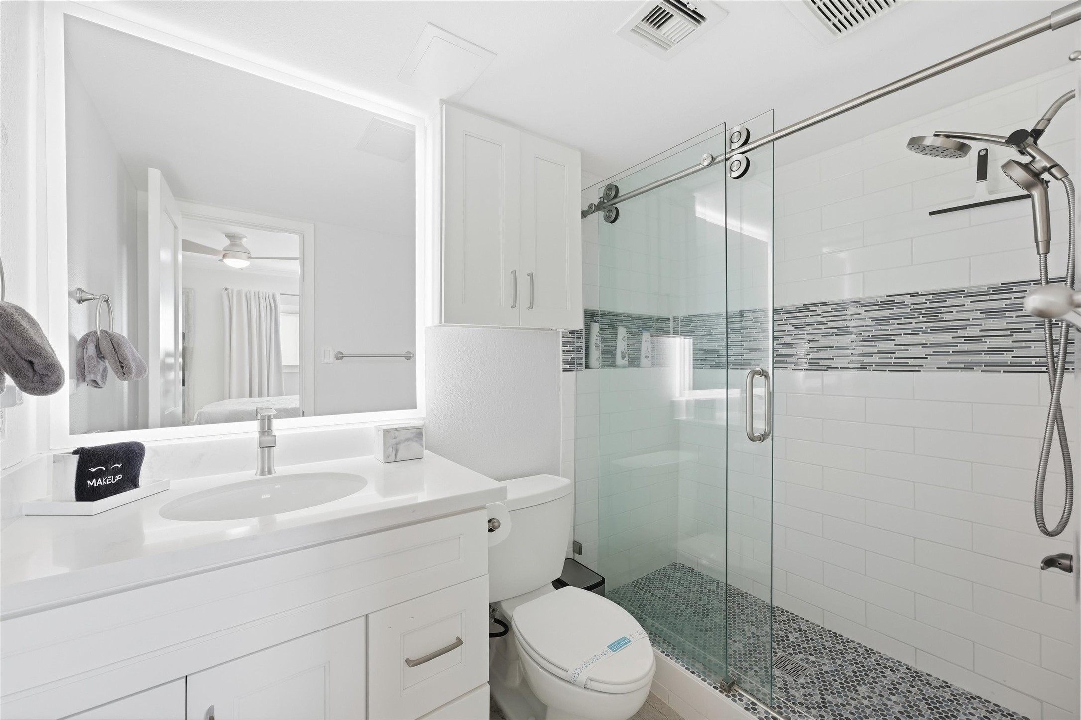 Bright and modern bathroom featuring a sleek glass-enclosed shower with stylish tile accents, a large mirrored vanity, and ample storage.