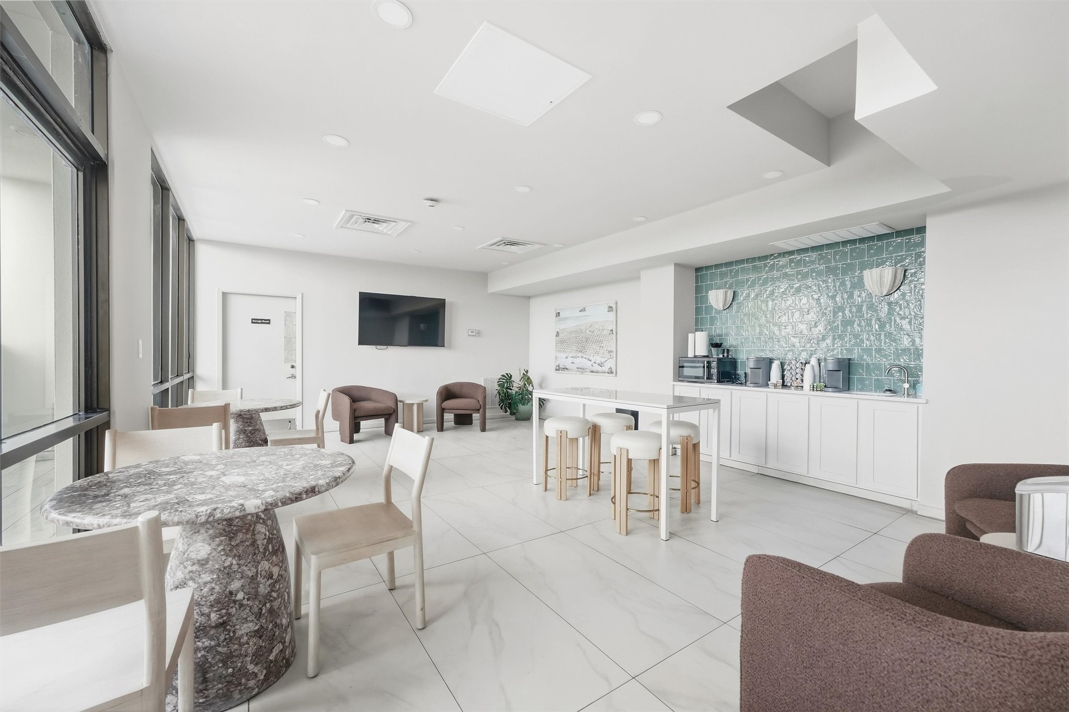 Bright and modern communal space featuring sleek tile floors, a cozy seating area, and a stylish kitchenette with a turquoise backsplash, perfect for socializing or enjoying a coffee.