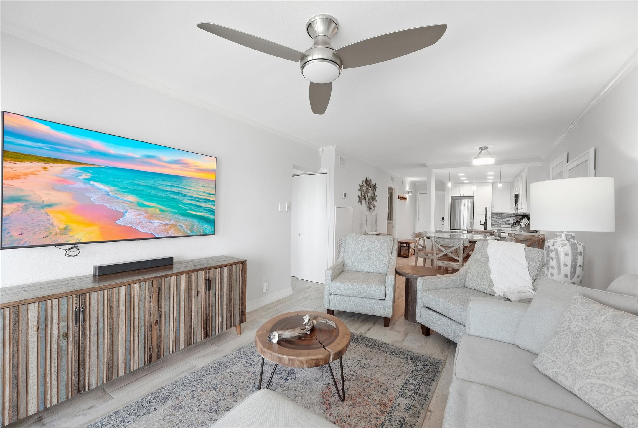 Bright and inviting living space featuring a stylish ceiling fan, cozy seating, and a vibrant wall-mounted TV. The open layout seamlessly connects to a modern kitchen, perfect for entertaining.