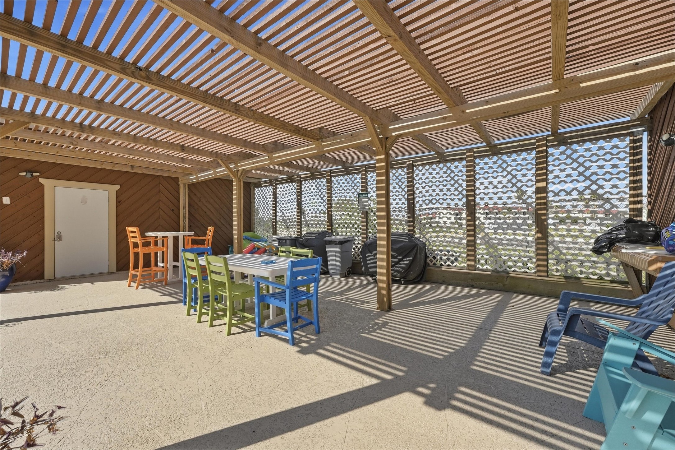 Spacious covered patio with a wooden pergola, colorful seating, and a built-in grill area, perfect for outdoor entertaining.