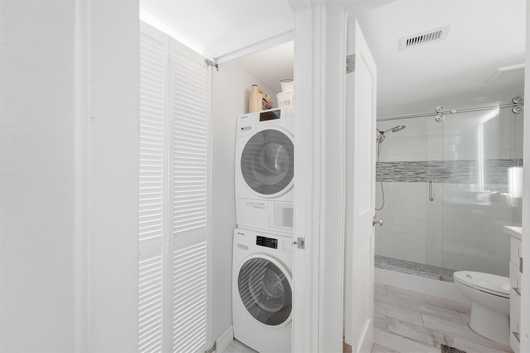 Convenient in-unit laundry with a sleek stacked washer and dryer set, adjacent to a modern bathroom featuring a glass-enclosed shower and updated tilework.