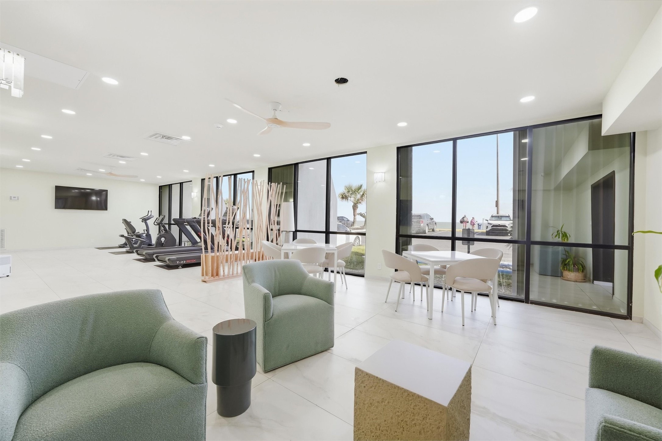 Bright and modern fitness and lounge area featuring large windows, comfortable seating, and exercise equipment, perfect for both relaxation and workouts.