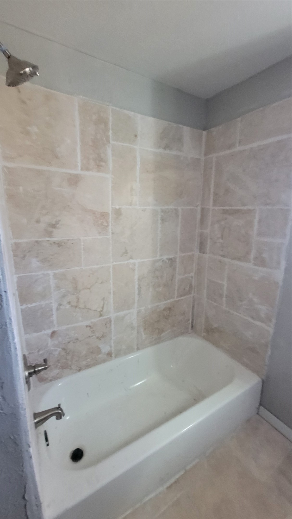This bathroom features a classic white bathtub with sleek fixtures, surrounded by beige tiled walls for a clean and neutral look.