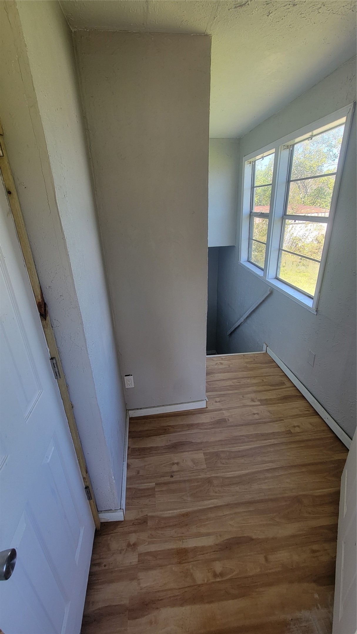 This photo shows a small landing area at the top of a staircase, featuring light wood flooring and large windows that provide natural light and a view of the outdoors.