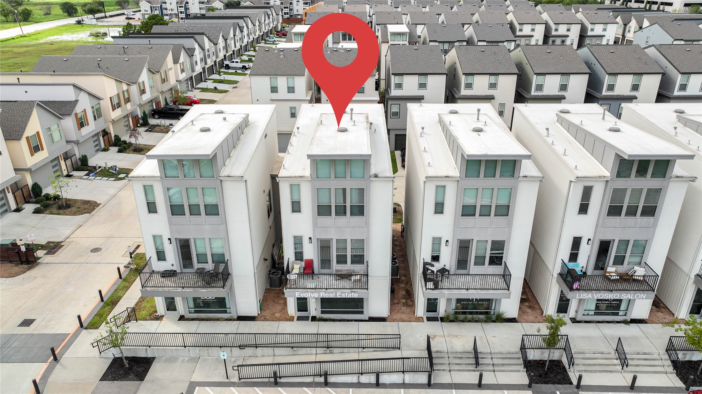 Modern three-story townhouse in a well-organized, urban neighborhood. Features include large windows, balconies, and a clean, contemporary design. The area is neatly landscaped and has convenient access to nearby amenities.