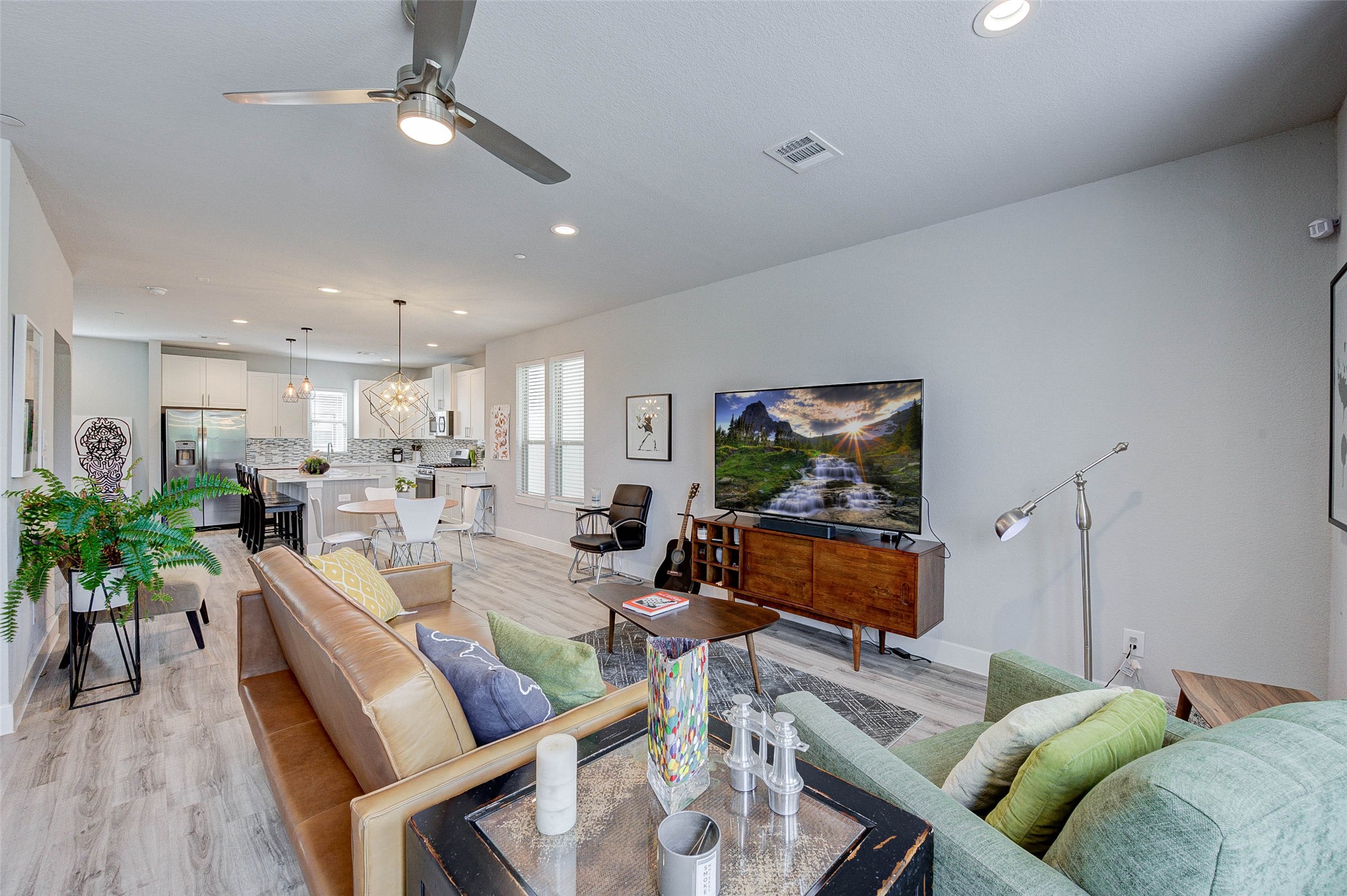 This modern, open-concept living space features a cozy seating area with a stylish sofa, a sleek entertainment setup, and a contemporary kitchen with a breakfast bar. The room is bright and airy, enhanced by recessed lighting and large windows. Perfect for comfortable living and entertaining.