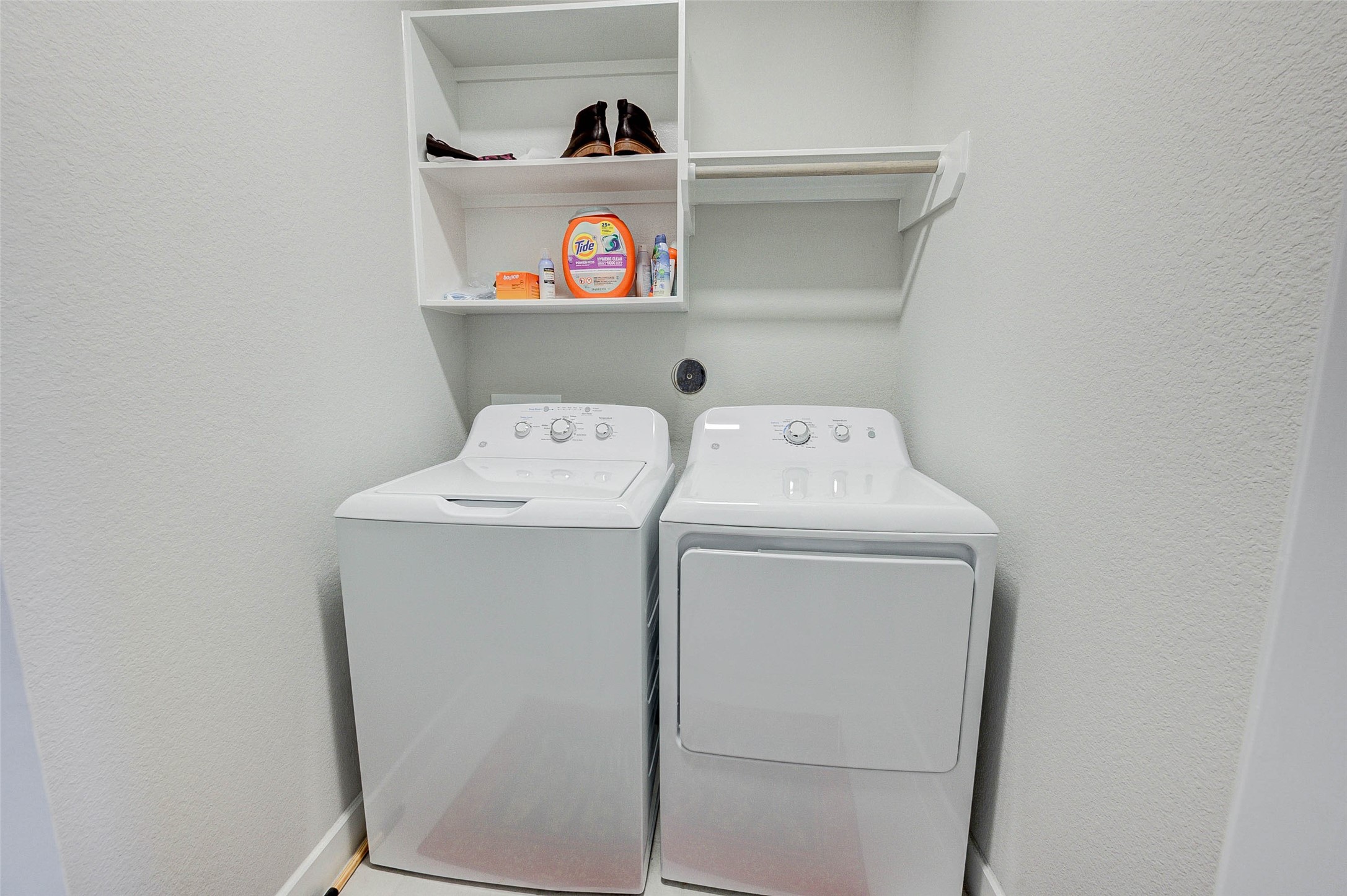 This photo shows a compact laundry area with a washer and dryer side by side. Above the appliances, there's shelving for storage, ideal for keeping detergents and laundry essentials organized. The space is clean and efficiently designed.