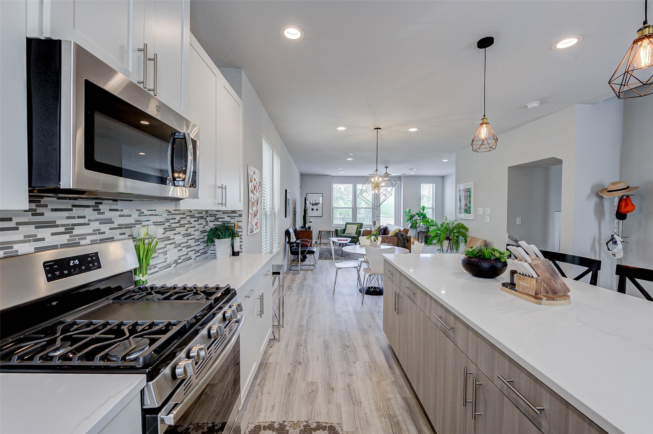 Modern kitchen with sleek stainless steel appliances, a spacious island, and elegant pendant lighting. The open layout extends to a bright living area with large windows, offering a welcoming and airy feel.