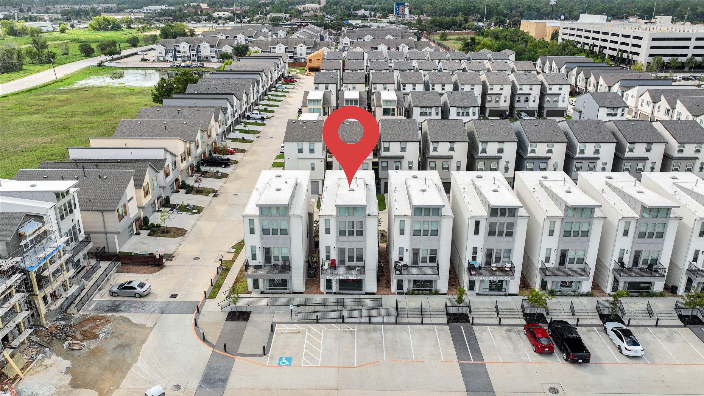 Modern row of white townhouses with clean lines and multiple stories, located in a well-organized residential community. The area appears spacious with parking and green surroundings, providing a suburban feel close to urban amenities.