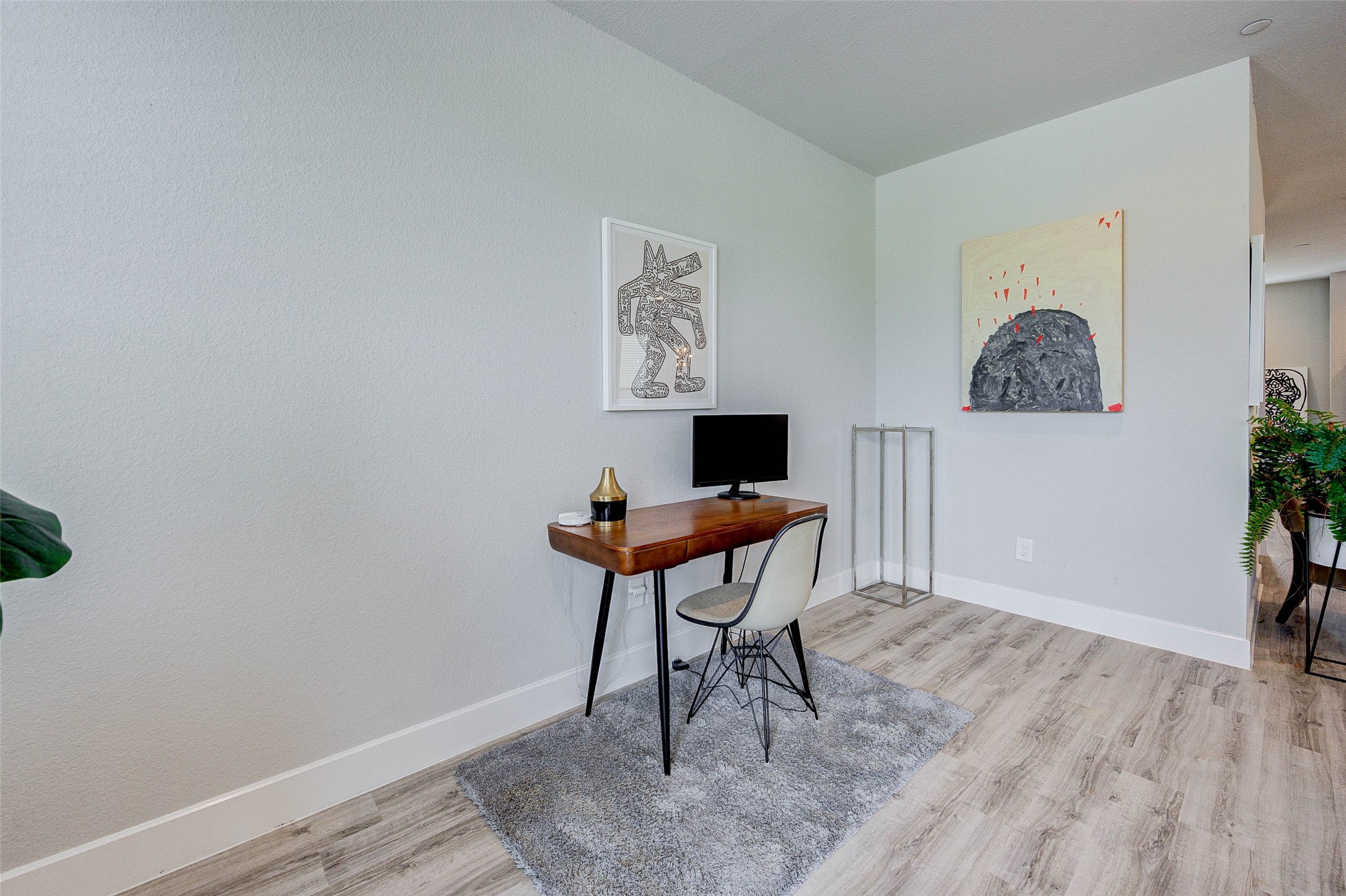 This photo showcases a modern home office space with light wood flooring and neutral walls. It features a sleek wooden desk with a computer, a stylish chair, and contemporary artwork on the walls. The room is bright, minimalist, and inviting, perfect for a productive work environment.