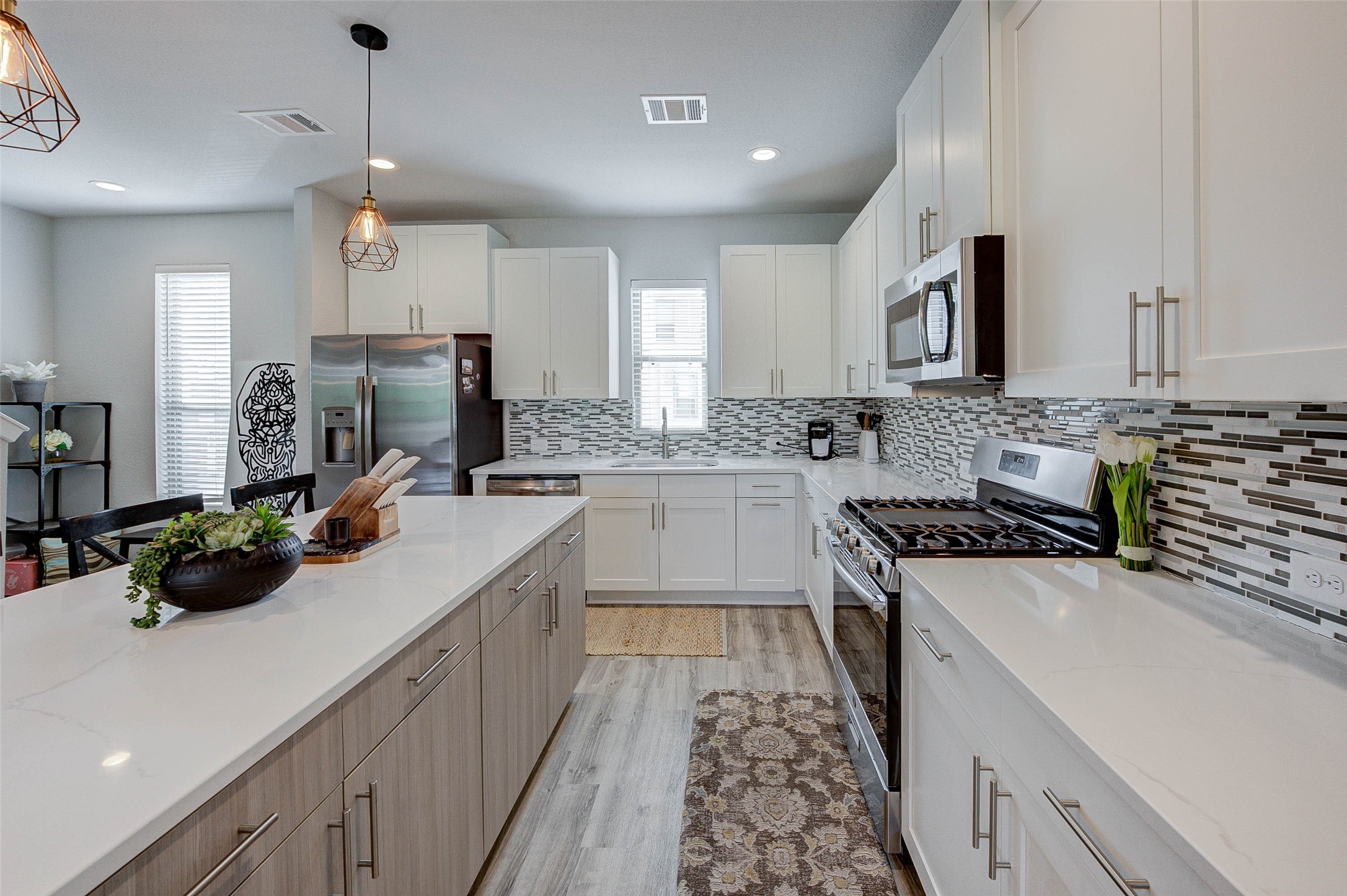 This modern kitchen features sleek white cabinetry, a stylish tile backsplash, and stainless steel appliances. It includes a spacious island with ample counter space and elegant pendant lighting, perfect for entertaining.