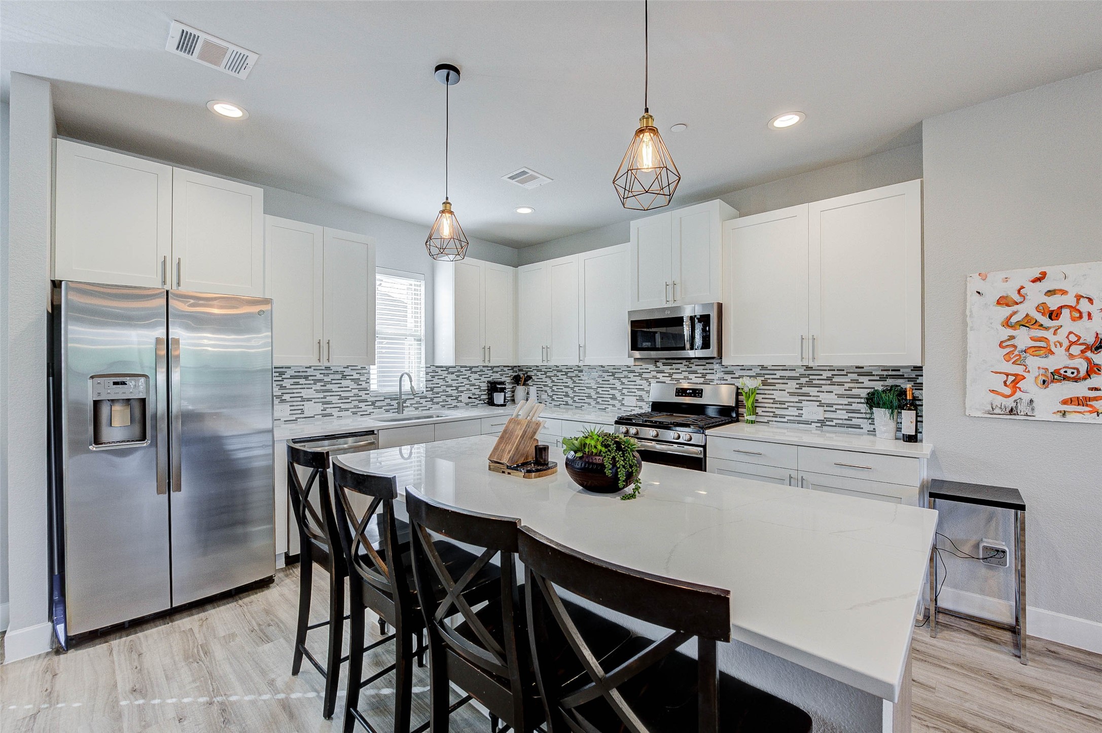 This modern kitchen features sleek white cabinetry, stainless steel appliances, and a stylish tile backsplash. The spacious island with pendant lighting offers additional seating and prep space, perfect for entertaining.