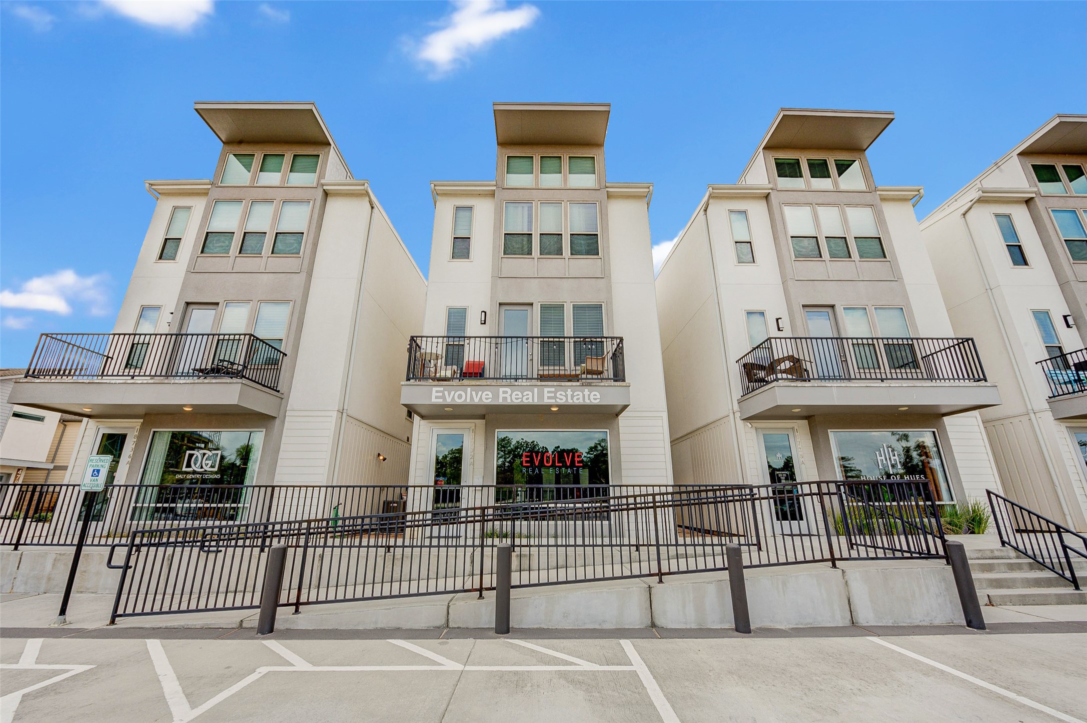 Modern multi-story townhouses with large windows and private balconies, featuring a central real estate office. The building has a clean, contemporary design with a welcoming entrance and ample parking space.