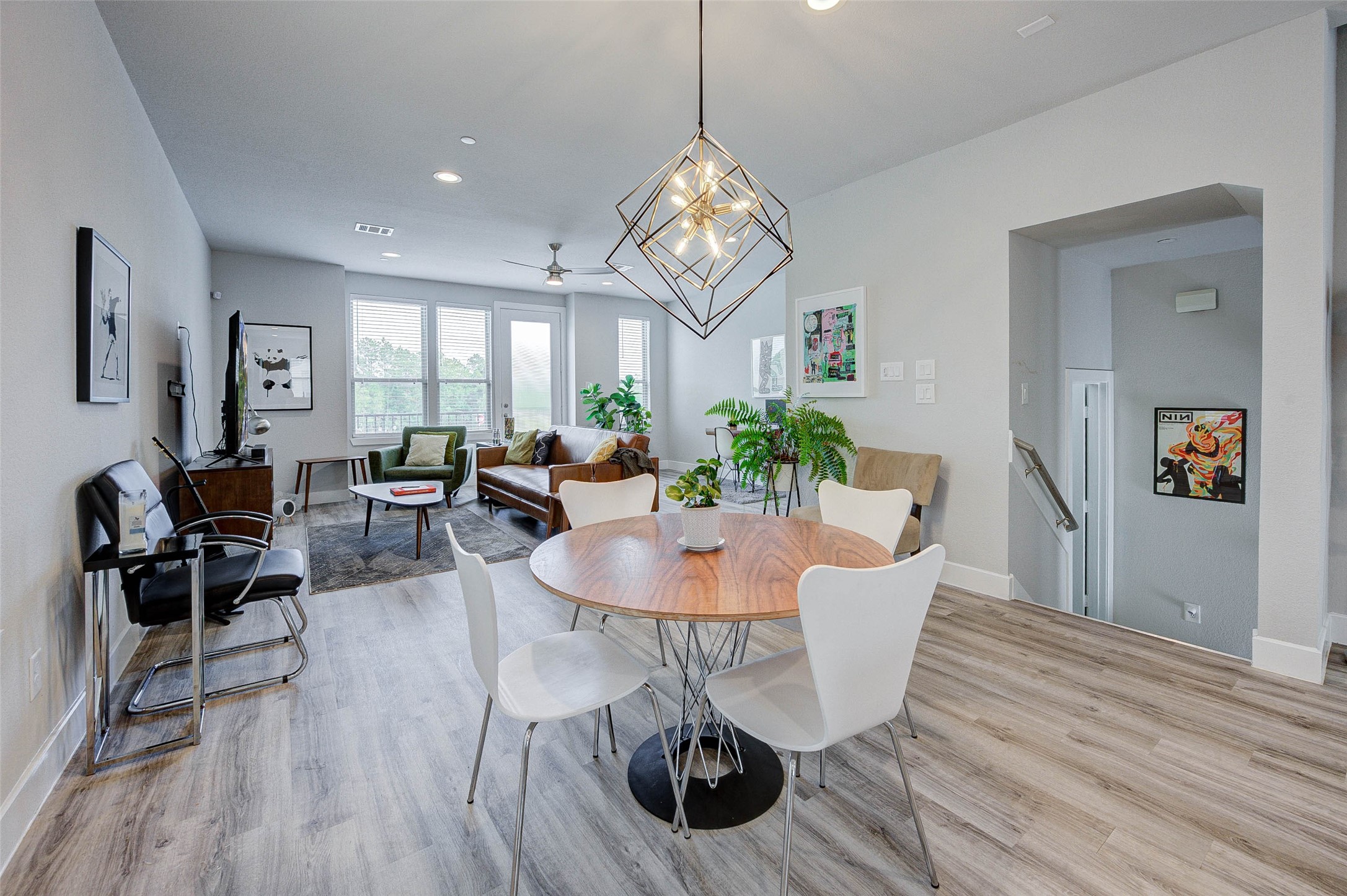 This modern living space features an open layout with a dining area, contemporary light fixture, and stylish decor. Natural light floods through large windows, highlighting the sleek flooring and comfortable seating area. Perfect for entertaining and relaxation.