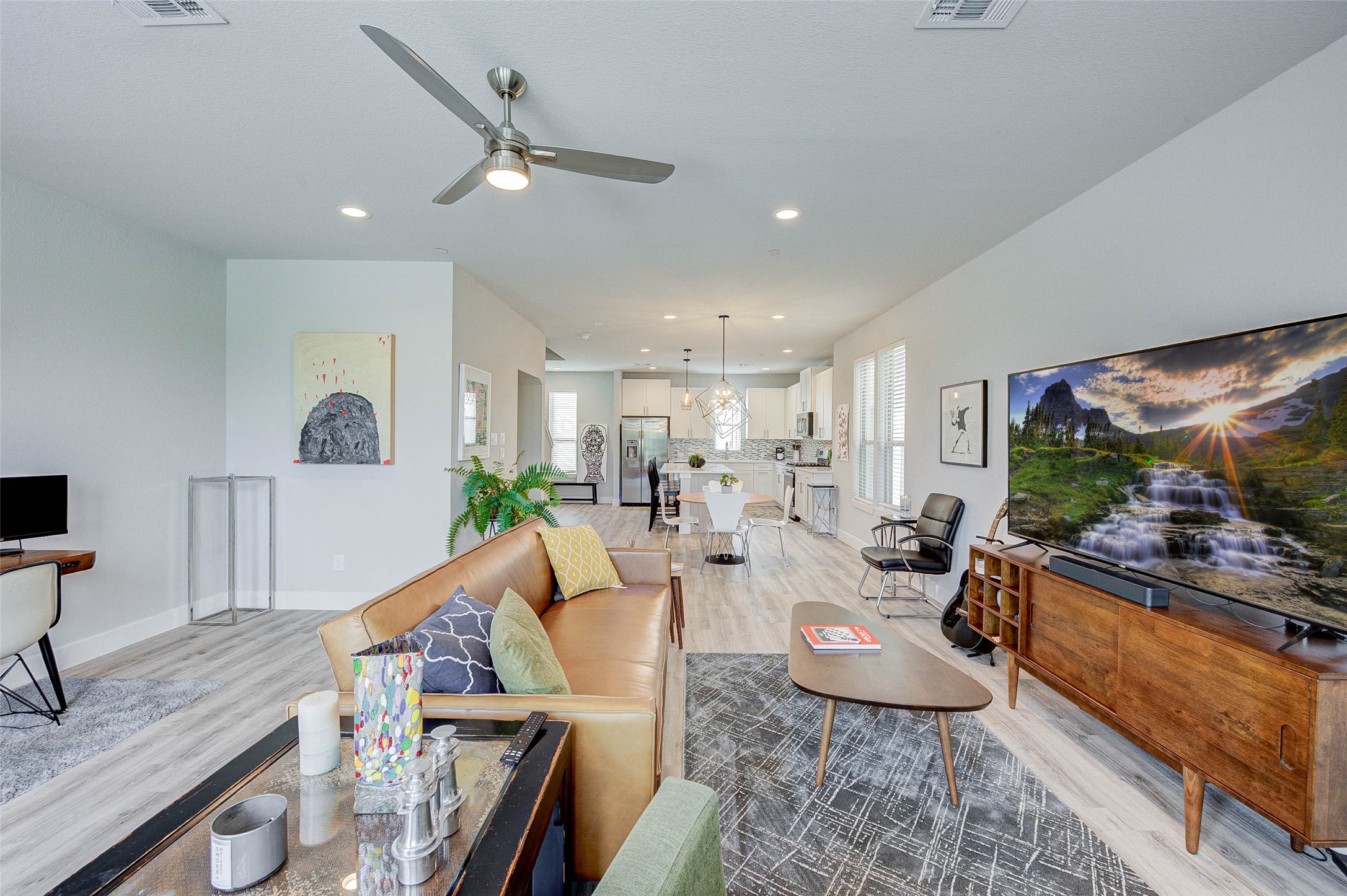 Spacious open-concept living area with modern design, featuring a cozy seating area, stylish decor, and a large TV. The room flows into a bright kitchen and dining space, highlighted by sleek appliances and contemporary lighting. Ideal for entertaining and family gatherings.