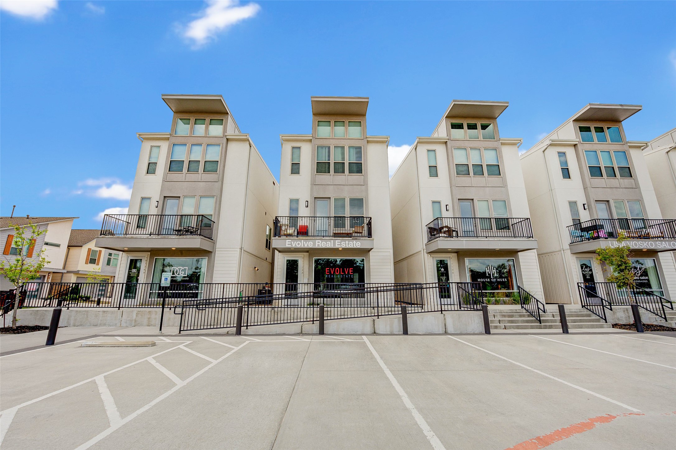 Modern townhouses with three stories, featuring large windows and balconies. The complex has a clean, contemporary design with a spacious parking area in front. Ideal for urban living.