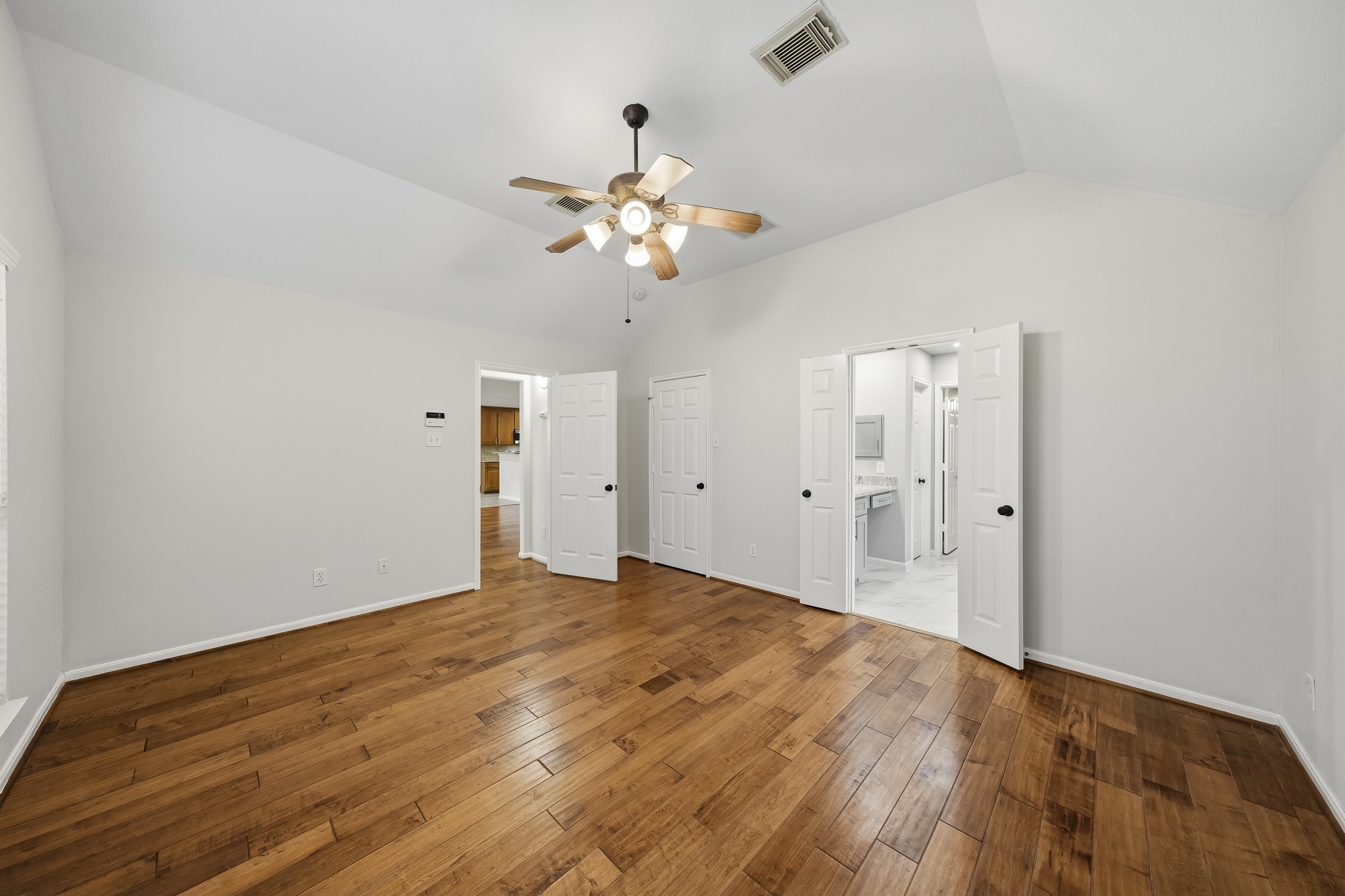 Spacious Spacious primary retreat with wood floors, vaulted ceiling, ceiling fan, and large windows that flood the room with natural light. This serene sanctuary offers ample space for a sitting area, walk-in closets, and an en-suite bathroom.