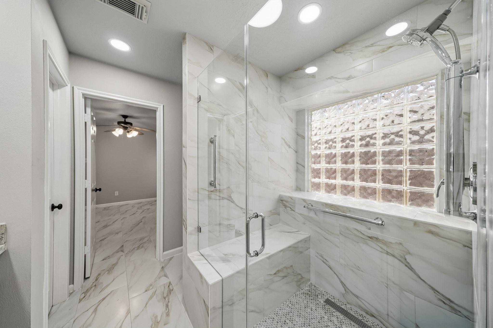Spacious walk-in shower featuring custom modern tilework, an integrated bench, and an elegant tile surround accented by a glass block window for natural light.