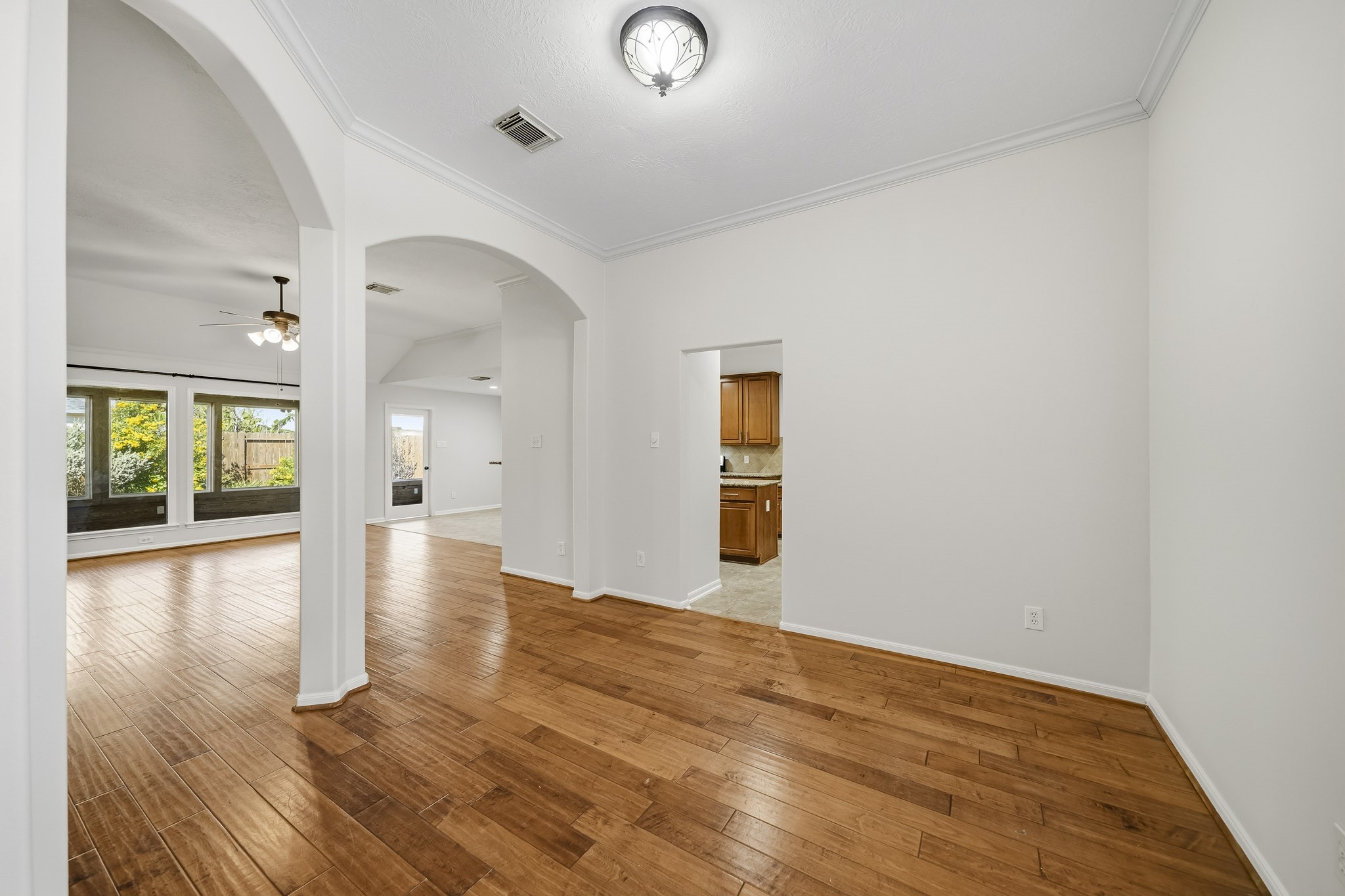Formal dining room featuring an open-concept flow into the main living area, accented by elegant arches, architectural columns, crown molding, and beautiful hardwood flooring.