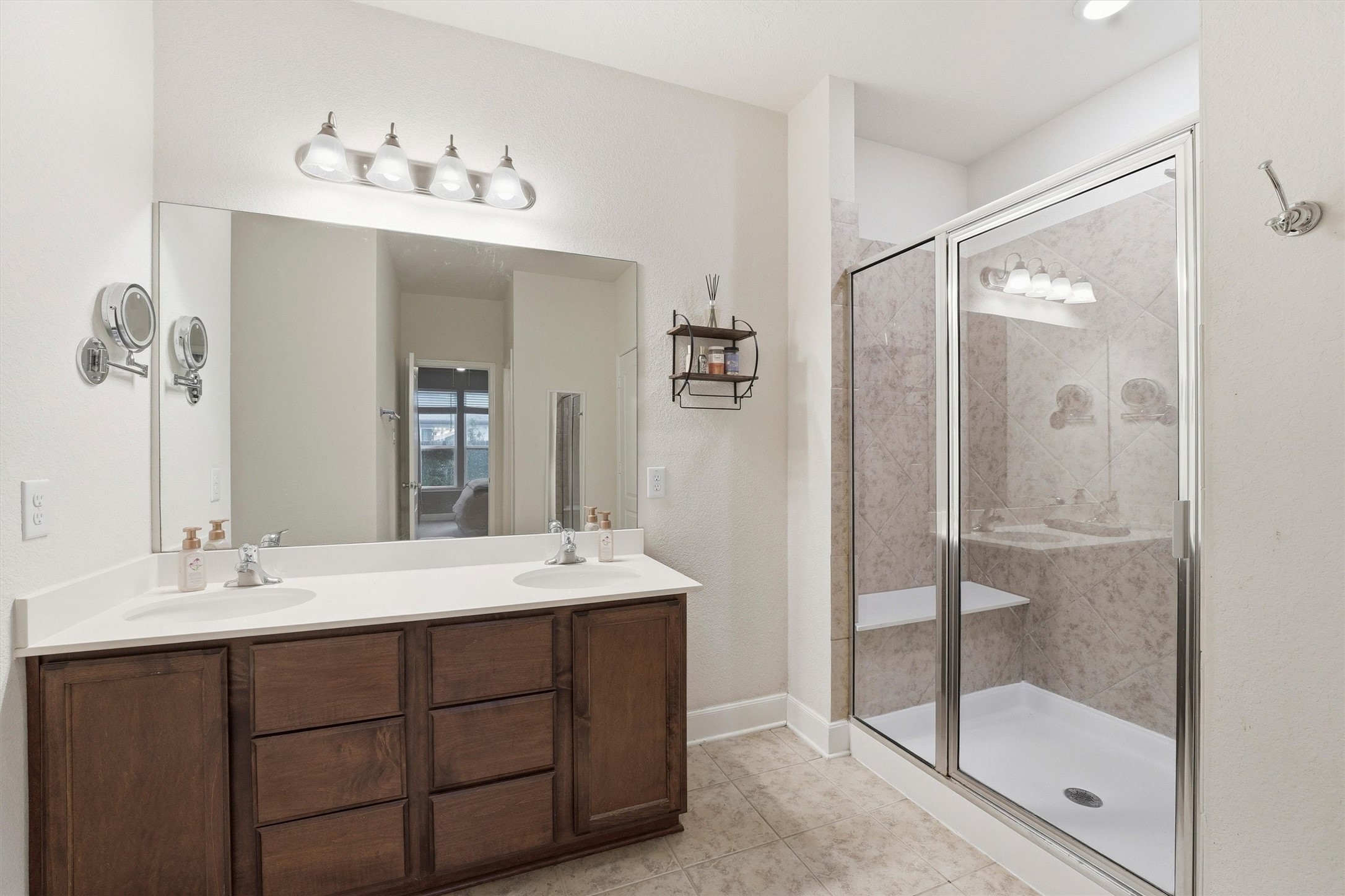 Well-designed primary bath with separate vanities, generous storage and a walk-in shower with tile surround.