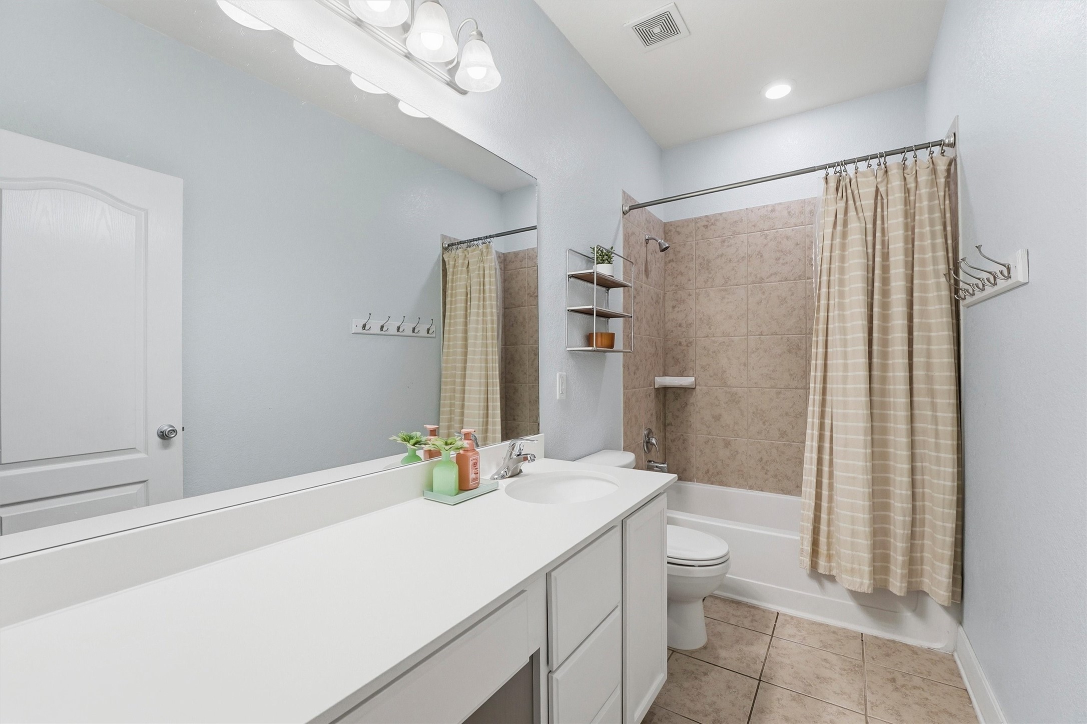 Full guest bathroom with a long vanity, neutral finishes and a tiled tub/shower surround.